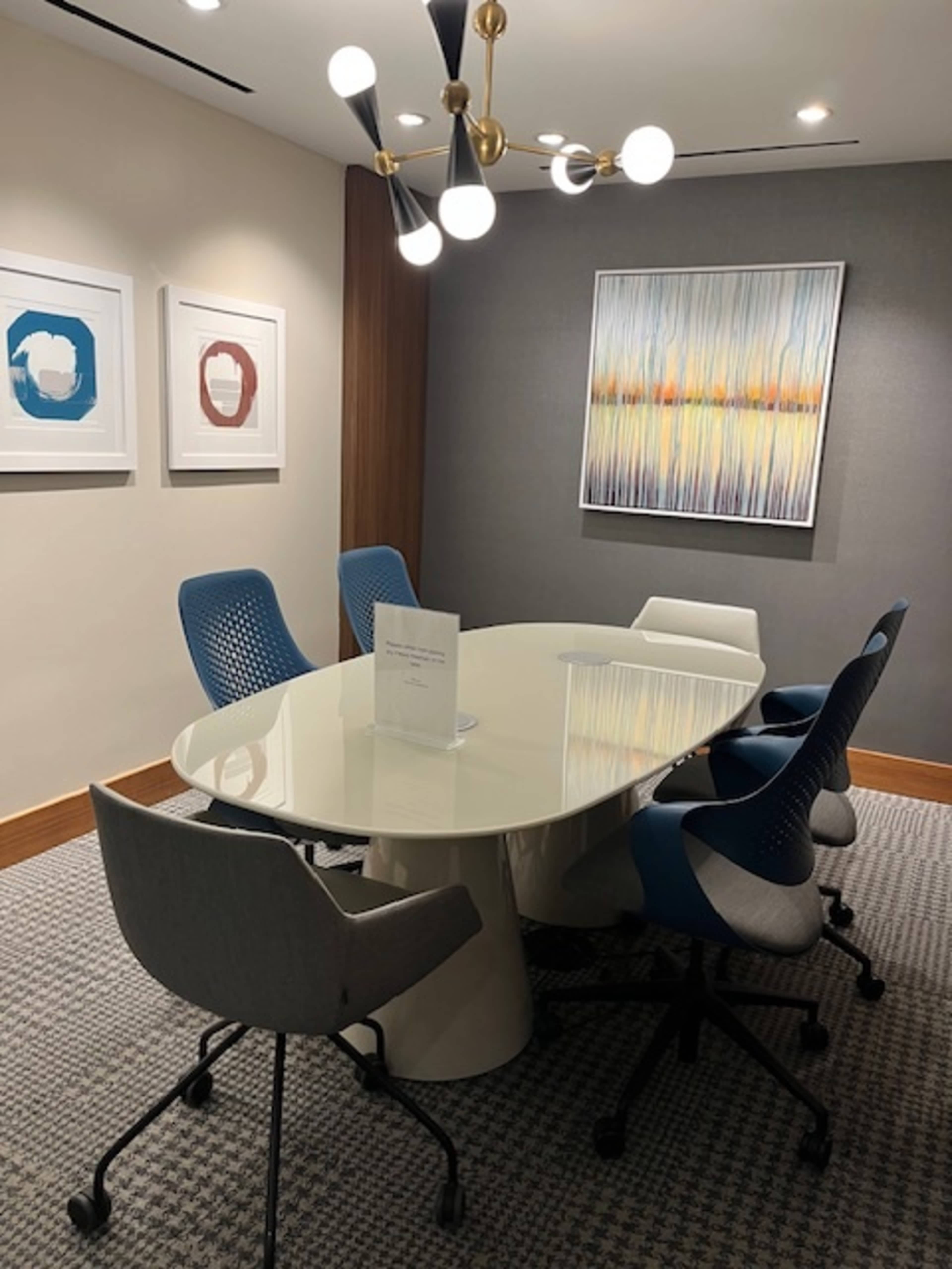 The image shows a modern conference room featuring an oval white table surrounded by six stylish chairs and artwork on the walls.