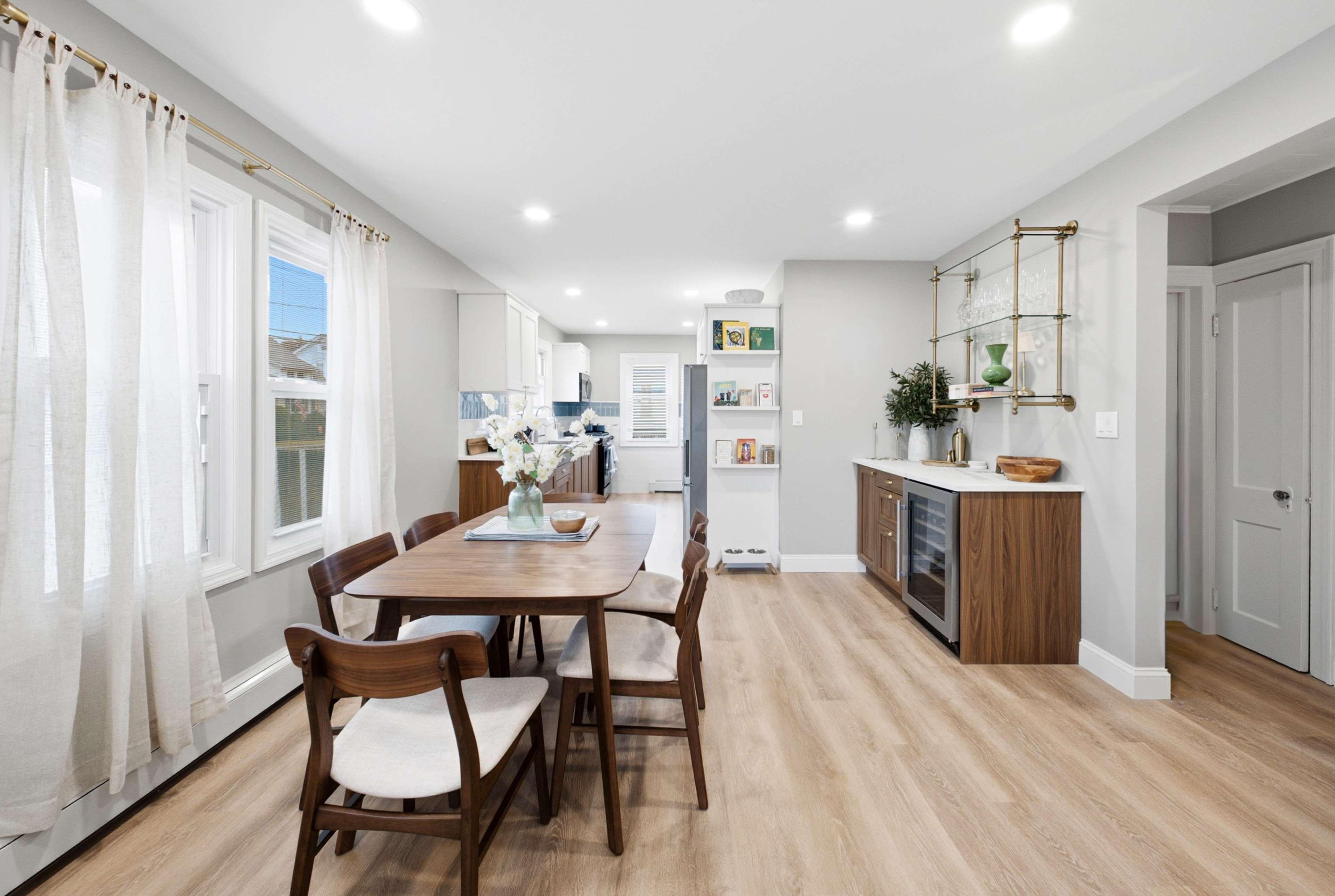 The image shows a modern kitchen and dining area with a wooden table, chairs, and a sleek layout featuring light-colored walls and cabinets.
