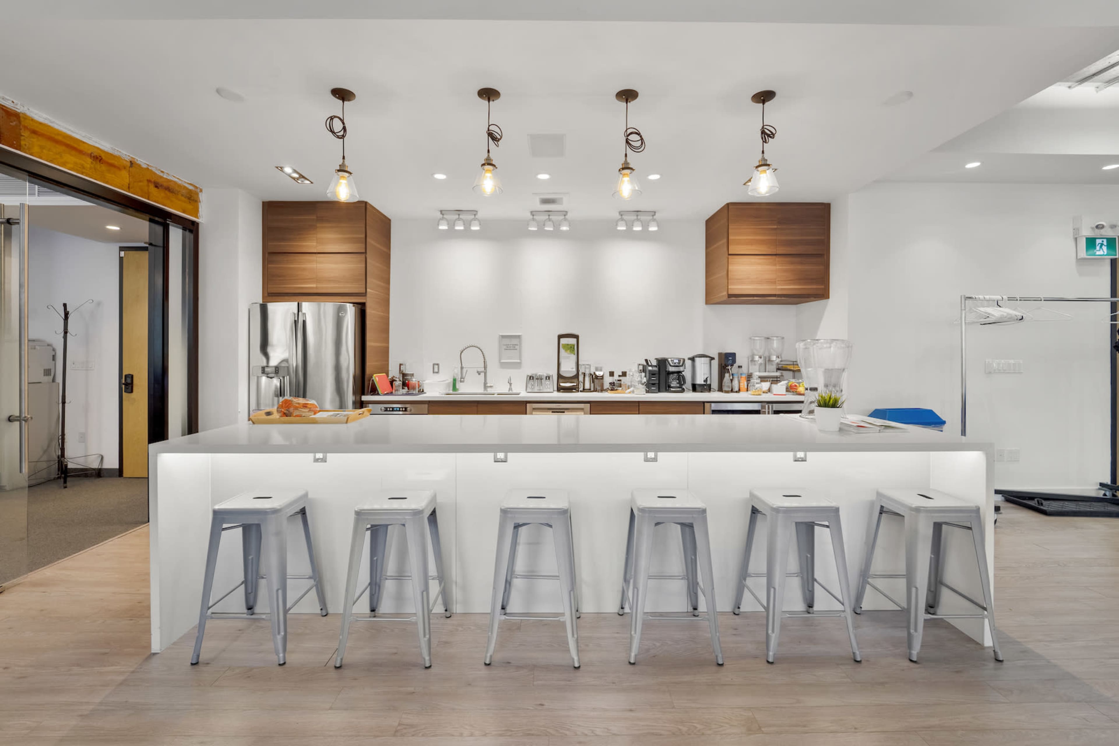 A modern kitchen features a large island with six metal stools, sleek cabinetry, and various appliances and utensils on the countertop.