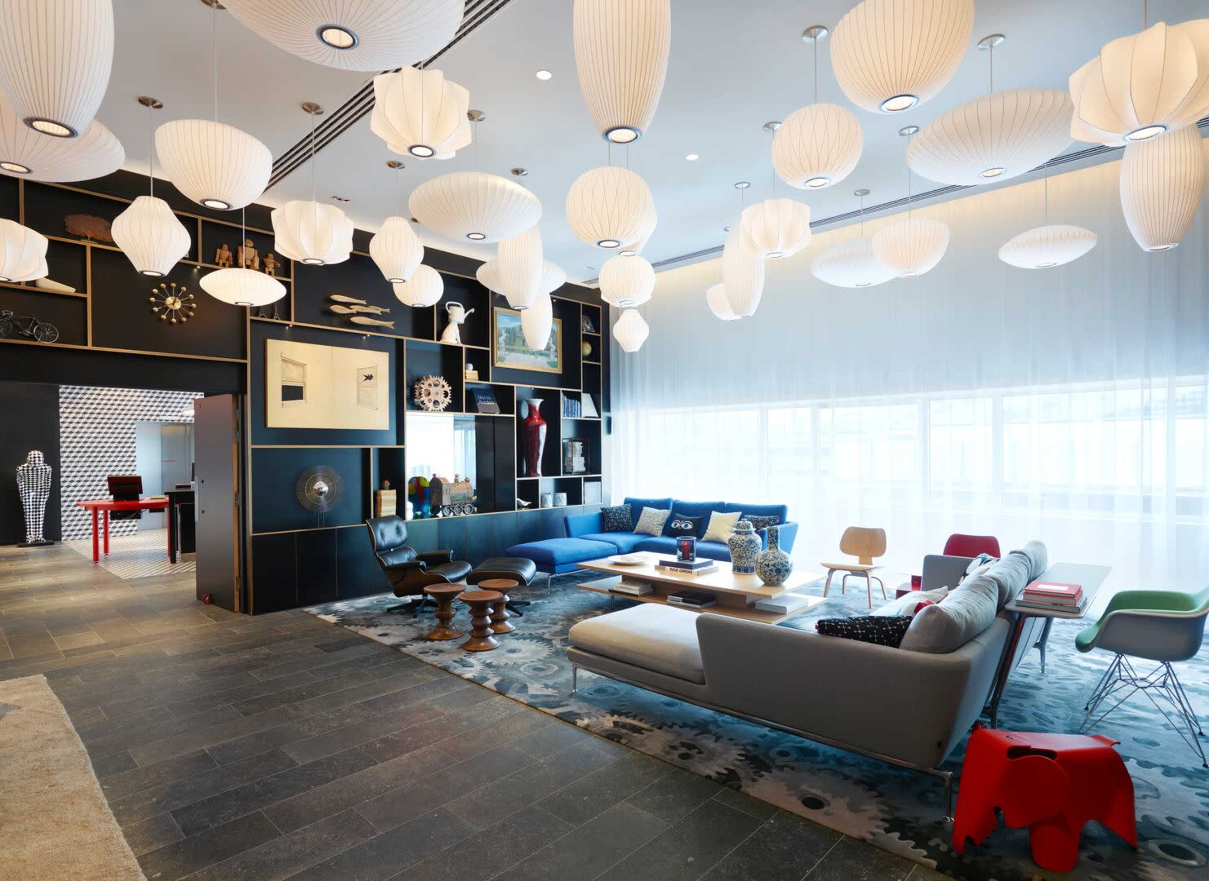A modern lounge area featuring an assortment of colorful furniture, decorative items, and pendant lighting.