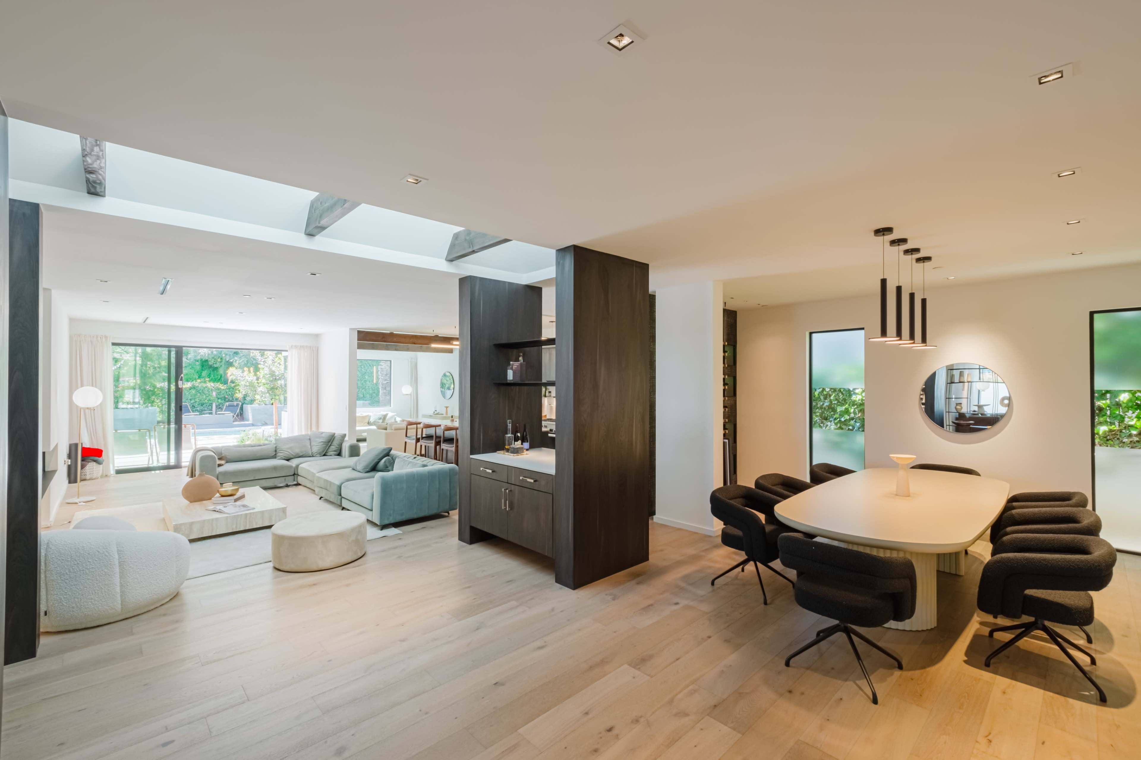 A modern open-plan living and dining area with minimalist furniture, large windows, and light wood flooring.