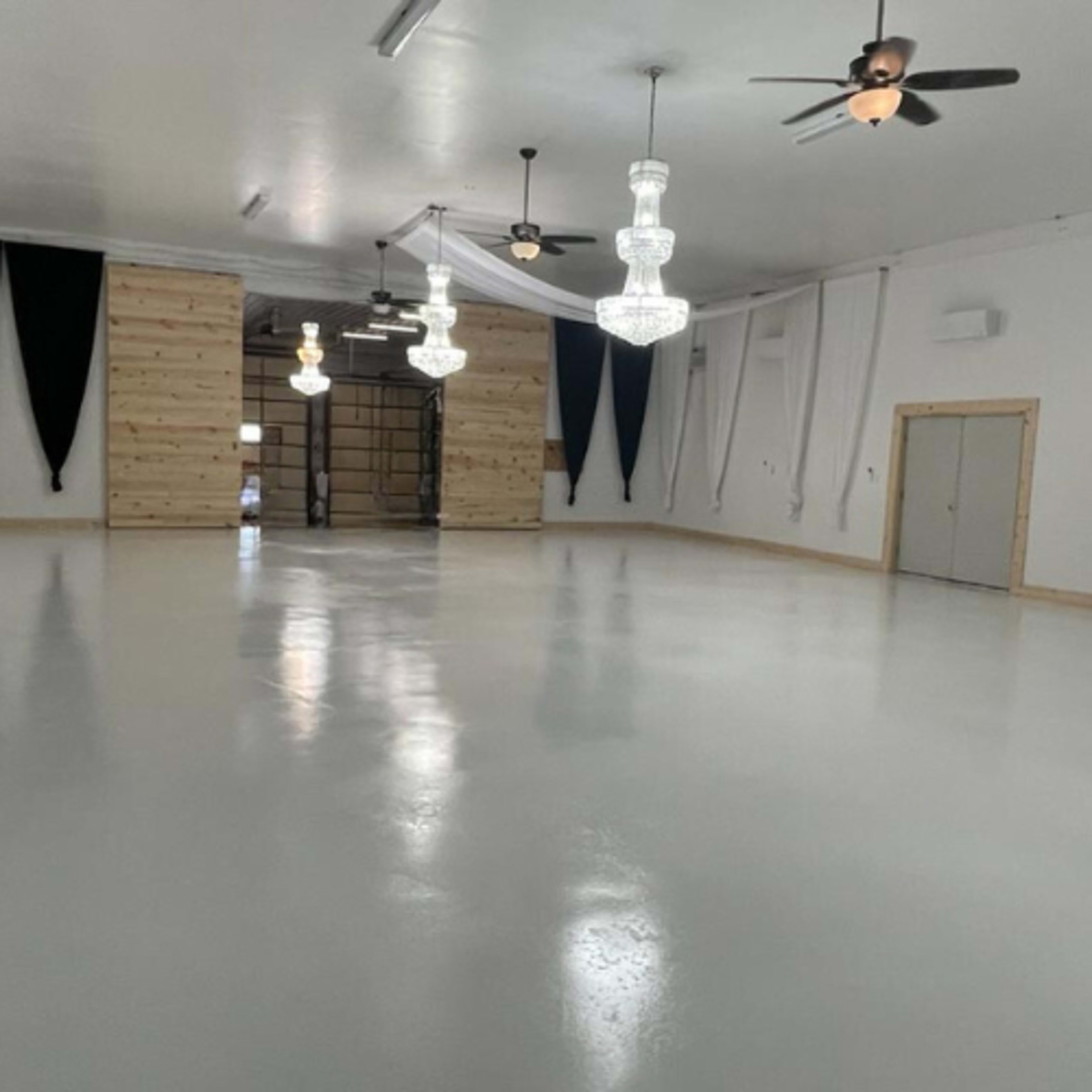 The image shows a spacious interior with a polished white floor, several chandeliers hanging from the ceiling, and wooden panels on one wall.