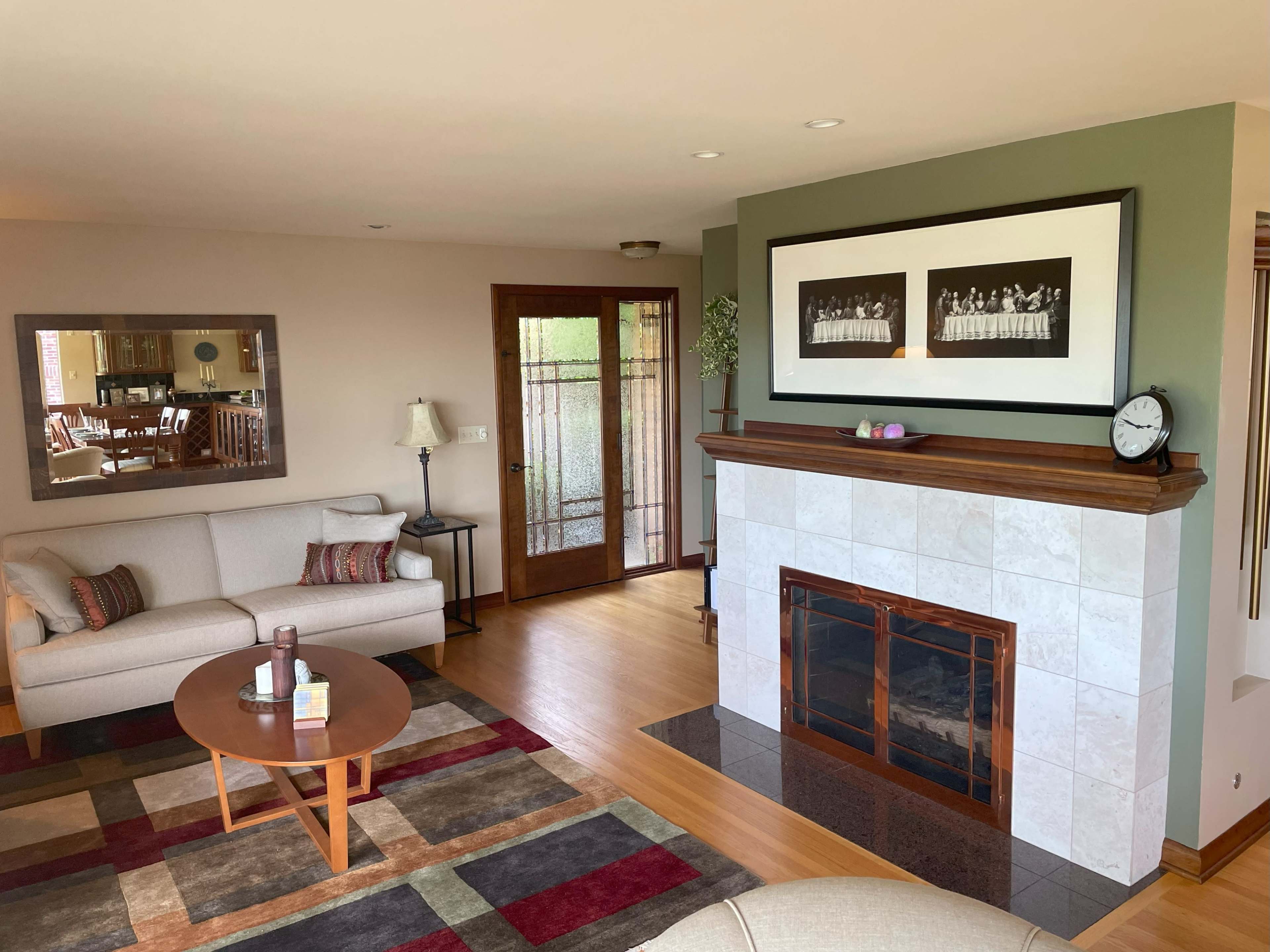 The living room features a beige sofa and a wooden coffee table, with a fireplace and a large mirror reflecting the space.