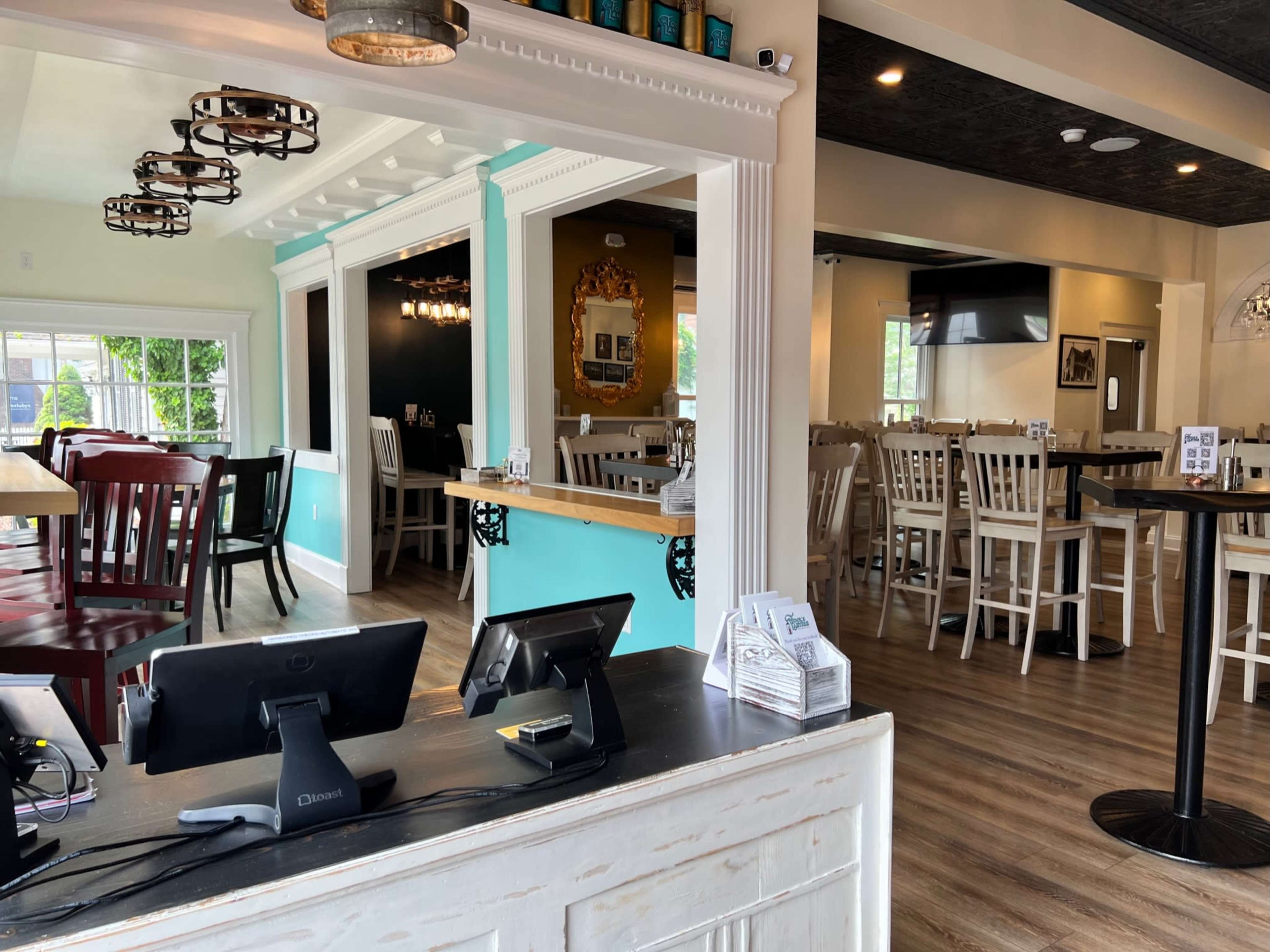 A modern cafe interior with wooden tables and chairs, large windows, and a counter area with stools.