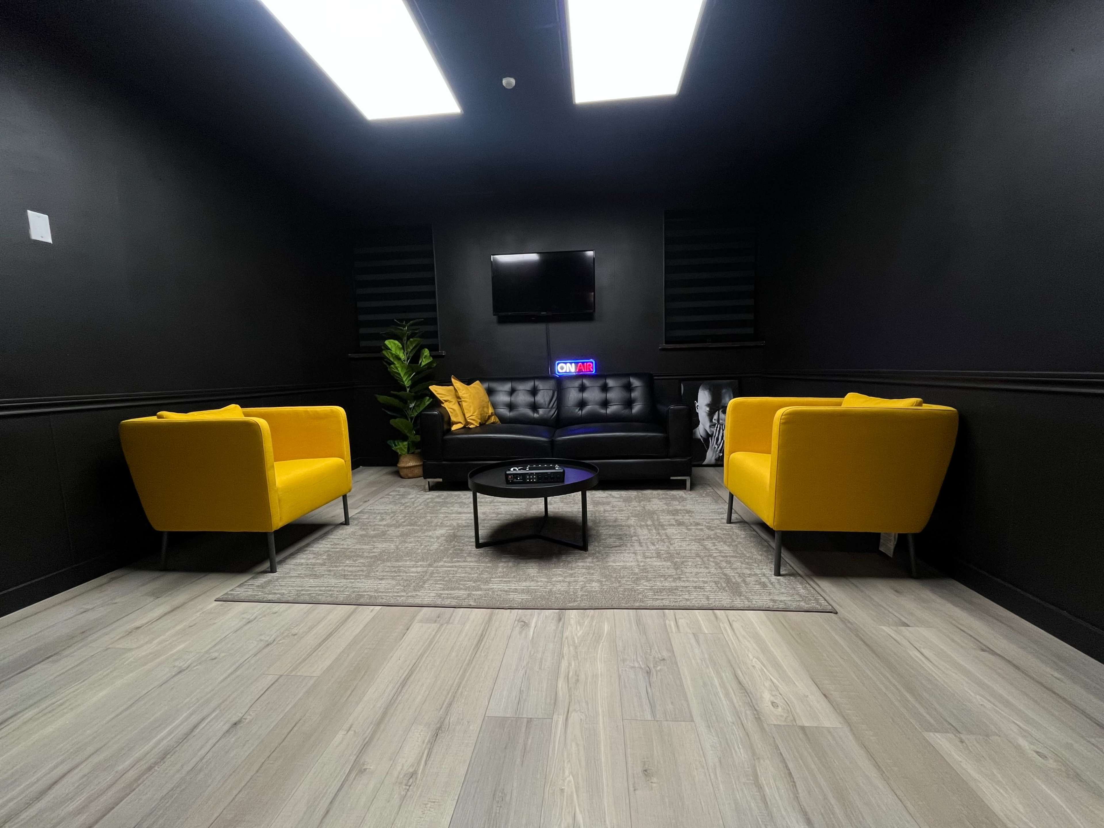 A modern lounge area with two yellow chairs, a black sofa, a small round table, and a plant against a dark backdrop.