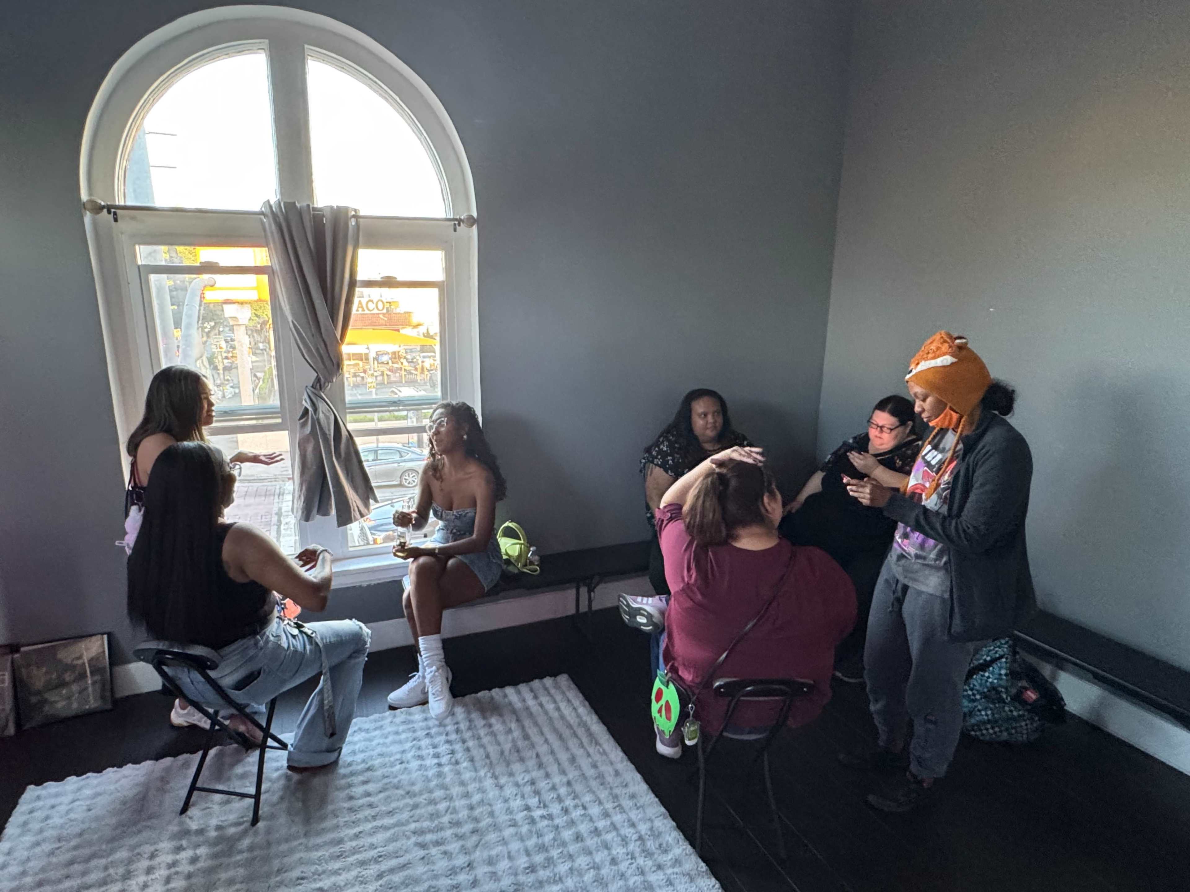 A group of seven individuals sits around in a well-lit room, engaging in conversation and sharing snacks.