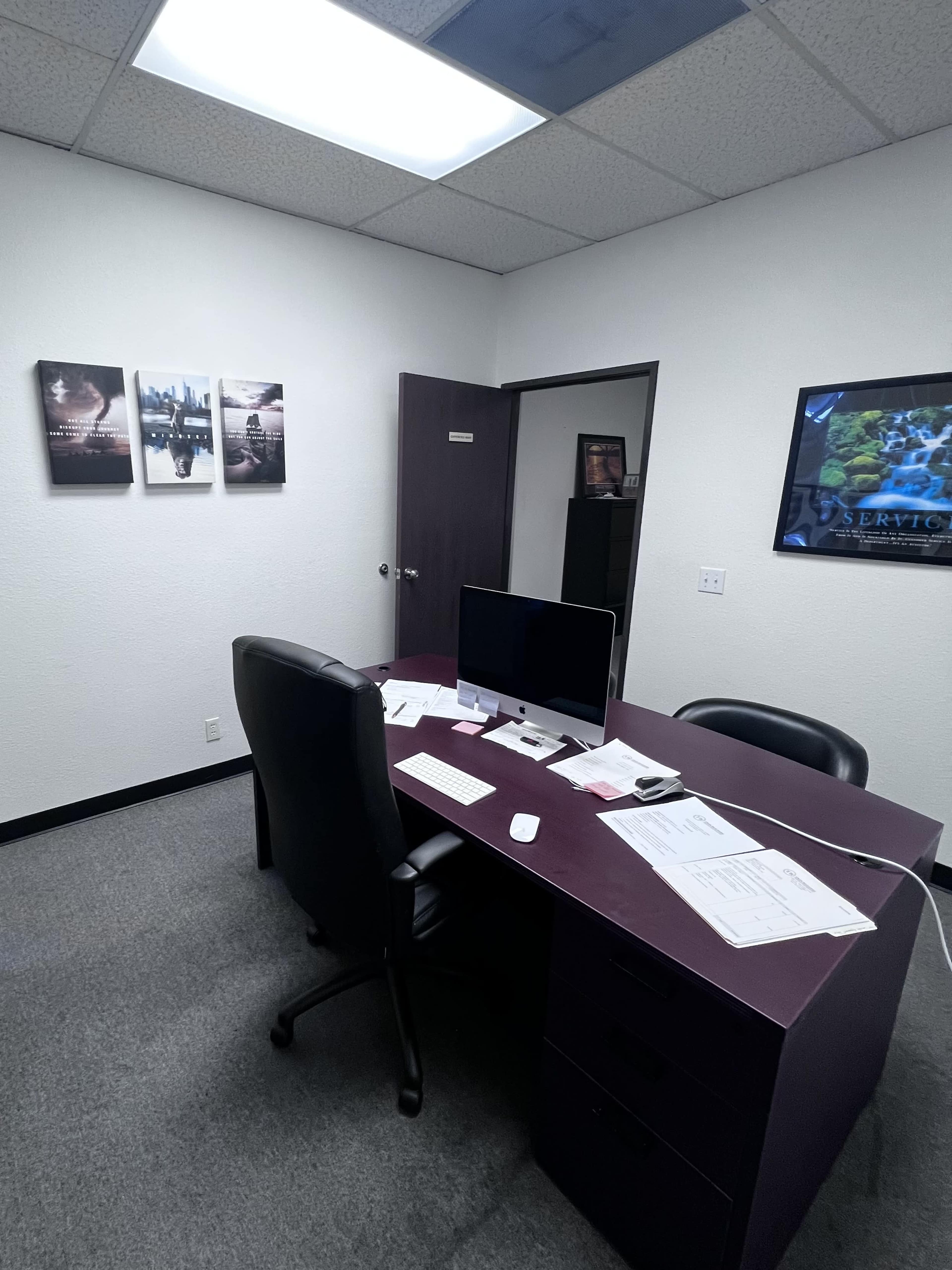 An office with a desk, an office chair, a computer monitor, and two framed pictures on the wall.
