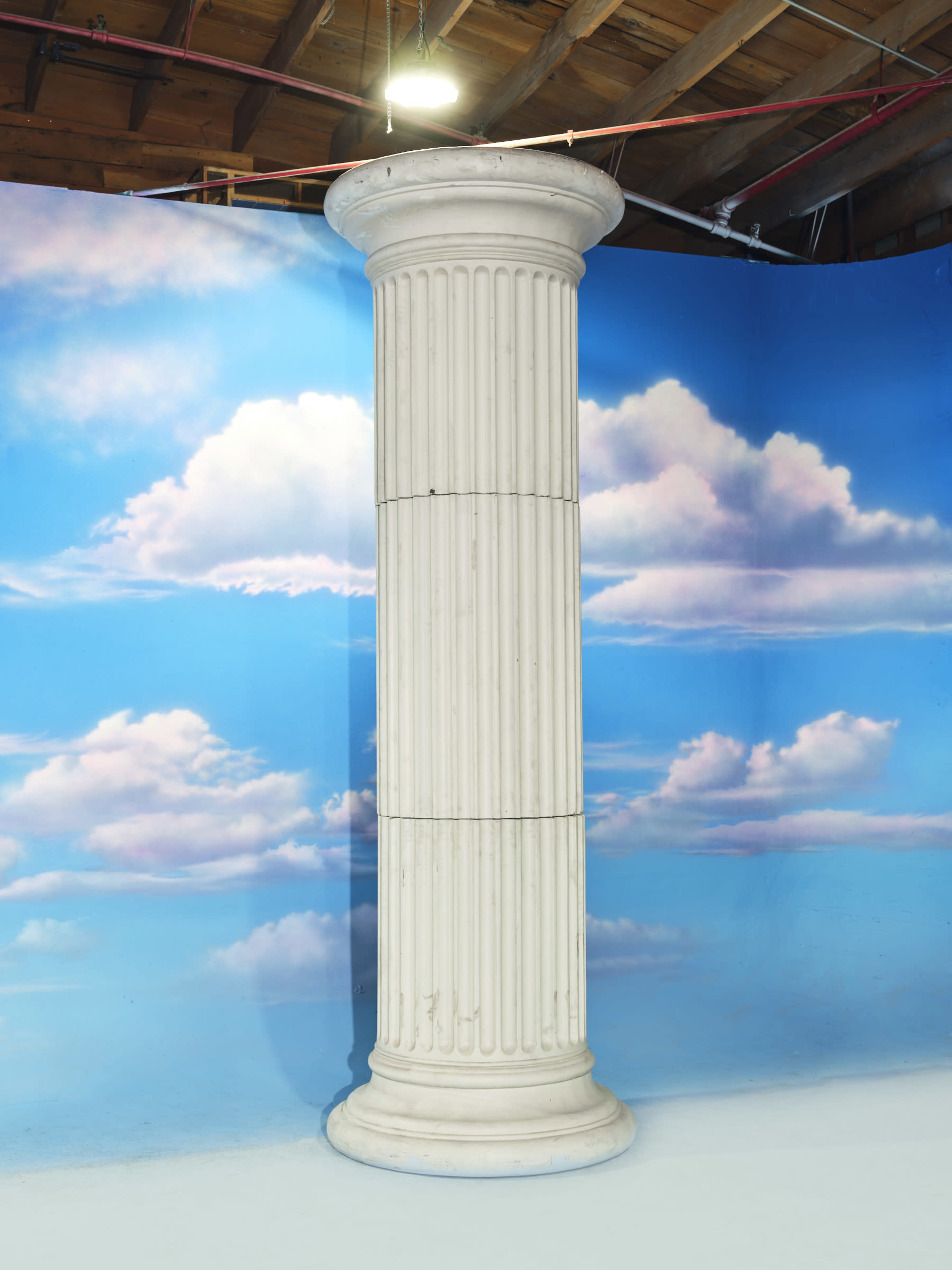 The image features a white, fluted column set against a blue backdrop with painted clouds.