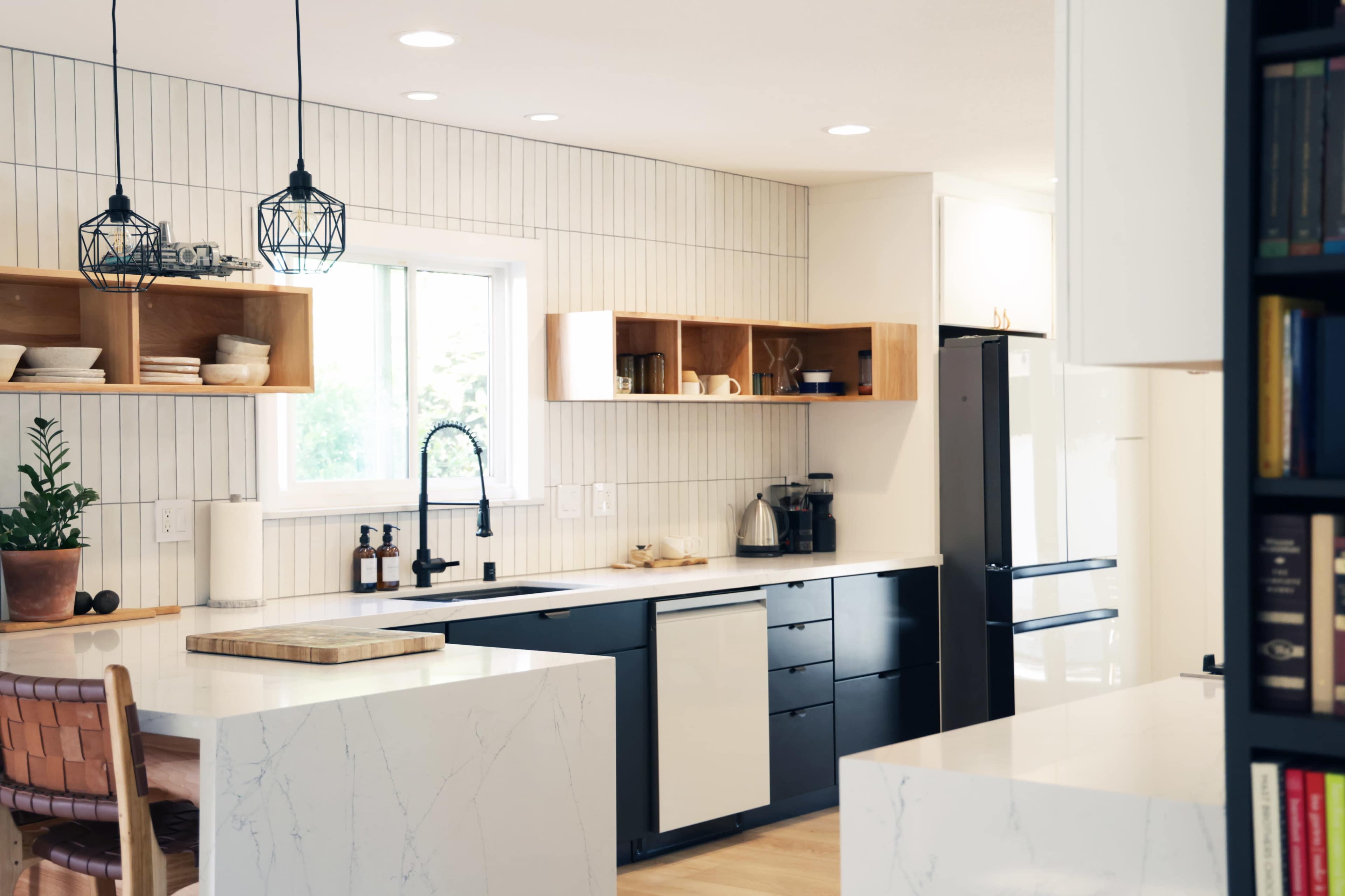 The kitchen features modern black cabinets, a large island with a marble countertop, and wooden shelves against light-colored walls.