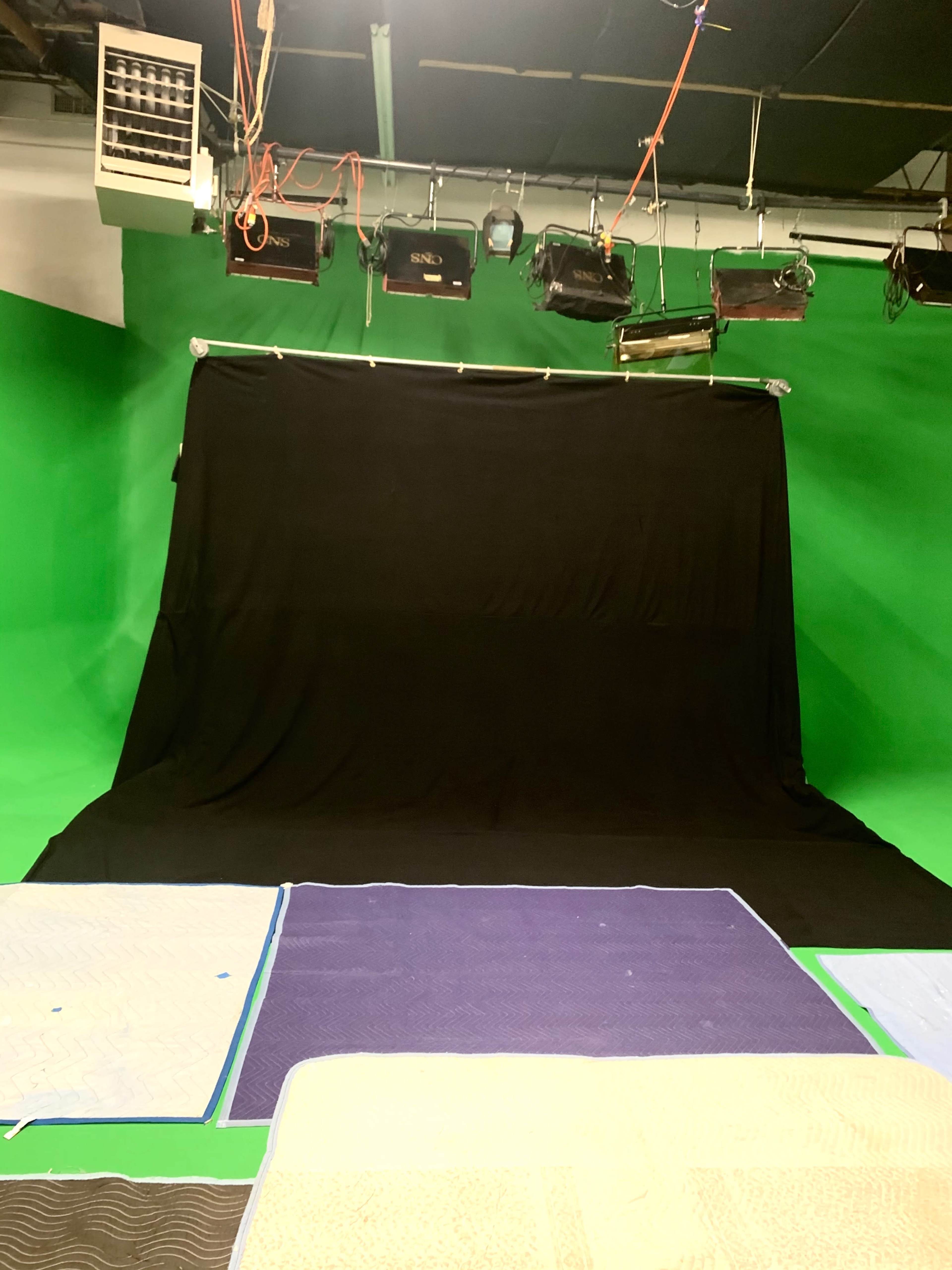 A studio setup with a black backdrop and green walls, along with several mats on the floor.