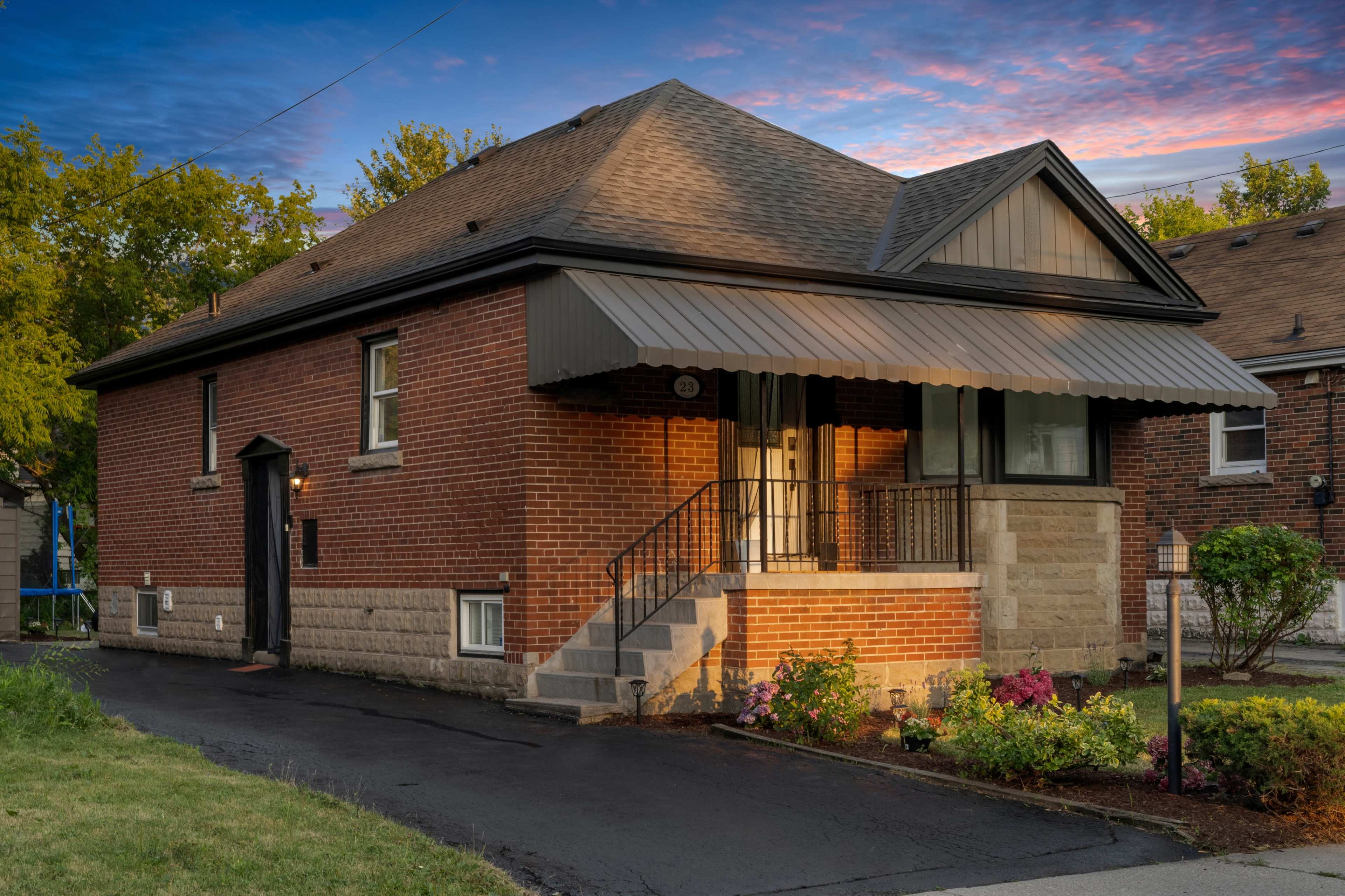 A brick house with a sloped roof, a front porch with steps, and landscaped flowerbeds in the yard.