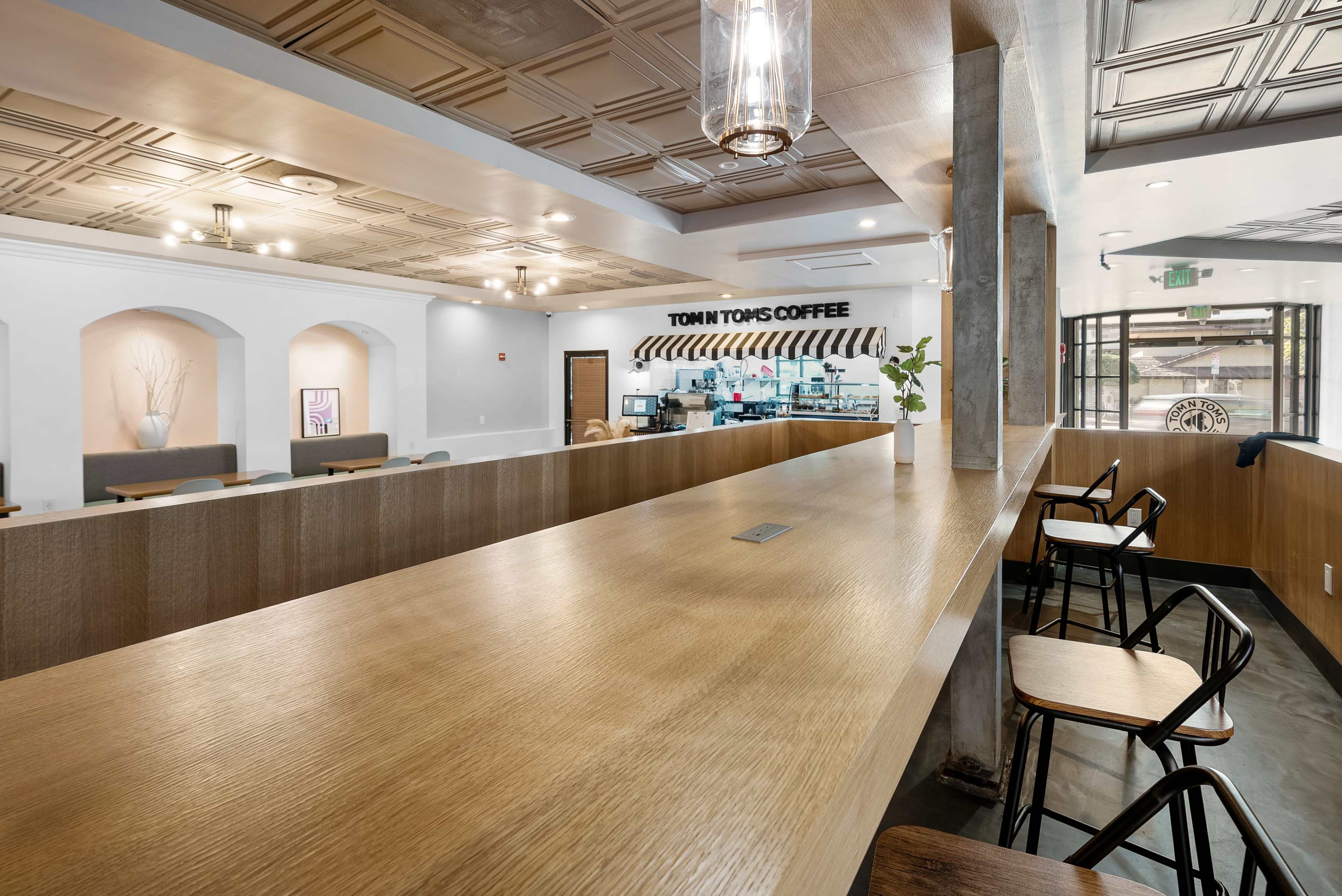 A modern coffee shop interior with a long wooden counter and seating areas, featuring a barista station in the background.