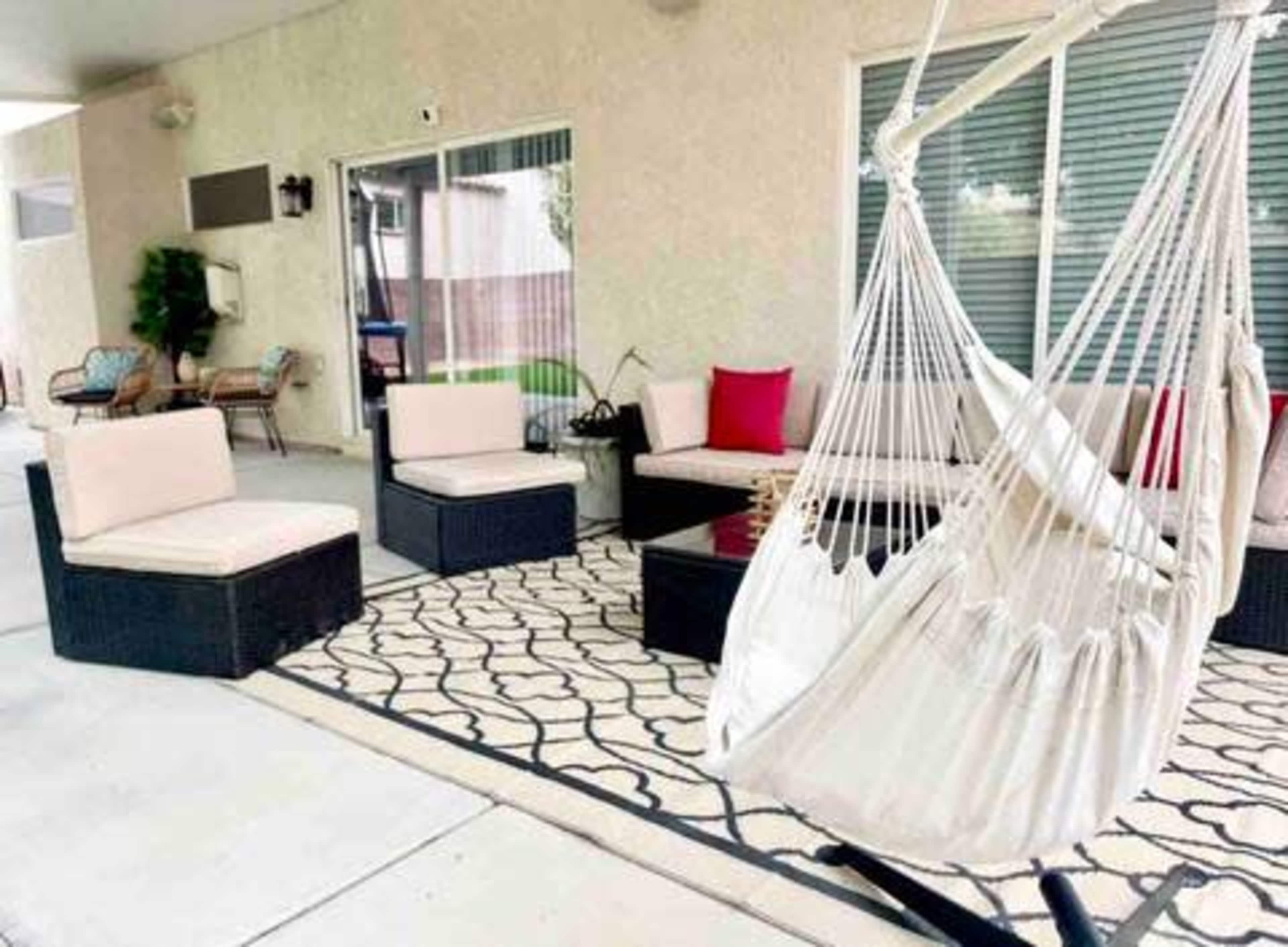 The image shows a cozy outdoor seating area with several cushioned sofas, a coffee table, and a hanging hammock, all arranged on a patterned rug.