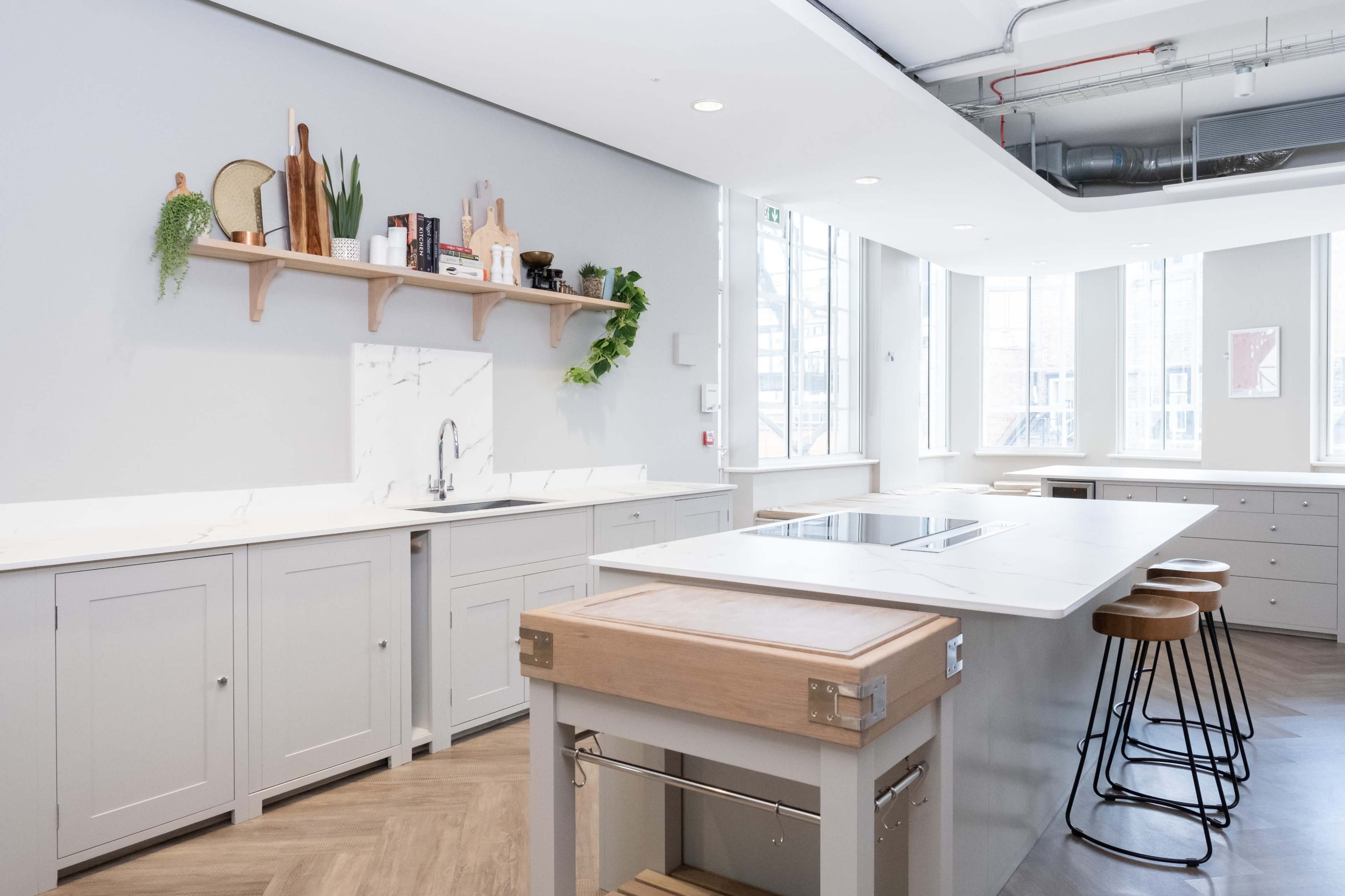 The image shows a modern kitchen featuring light gray cabinetry, a marble countertop, and a central island with bar stools.