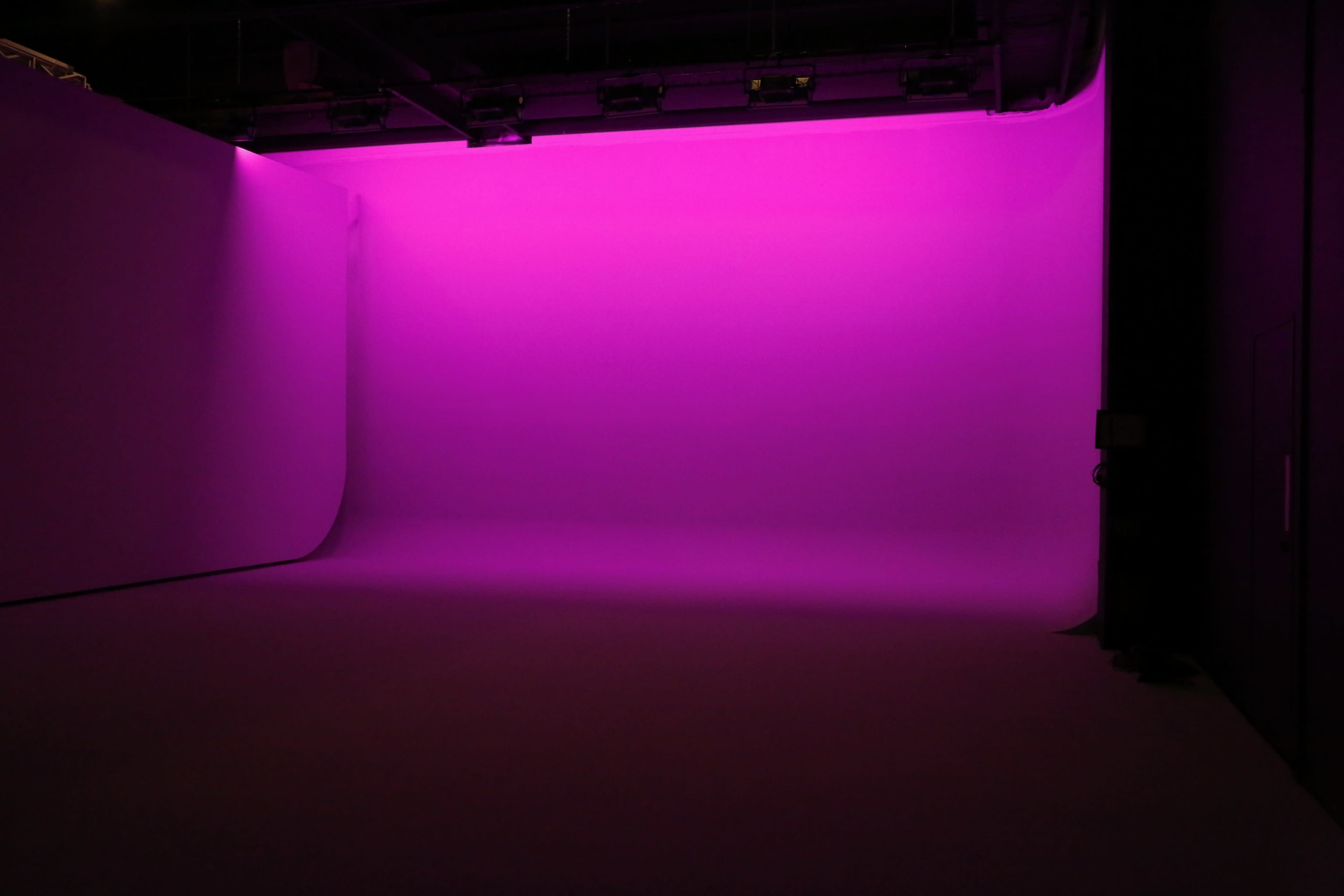 A studio interior with a seamless backdrop illuminated in bright pink light.