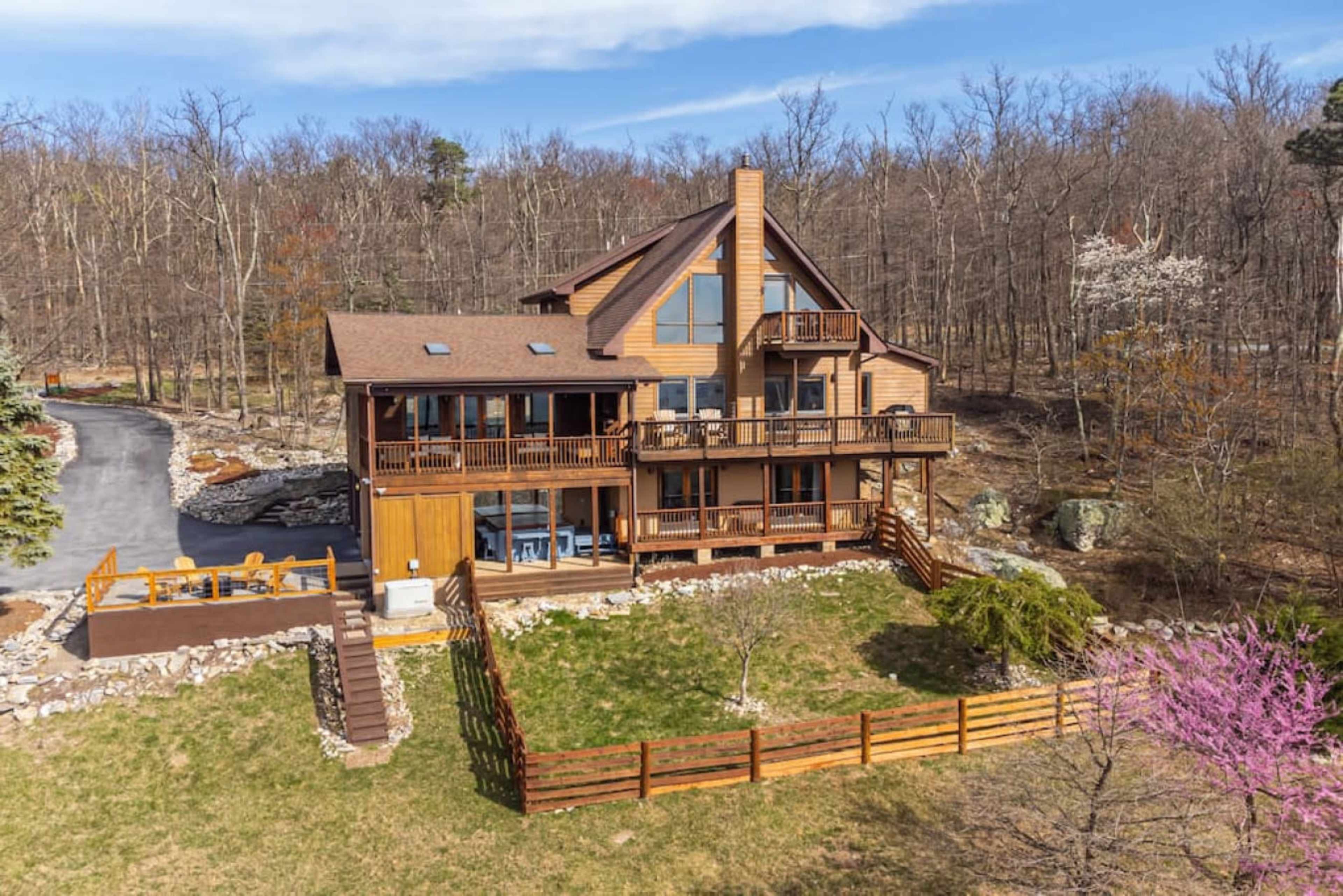 A large wooden house with multiple balconies and a deck overlooks a grassy yard surrounded by trees.