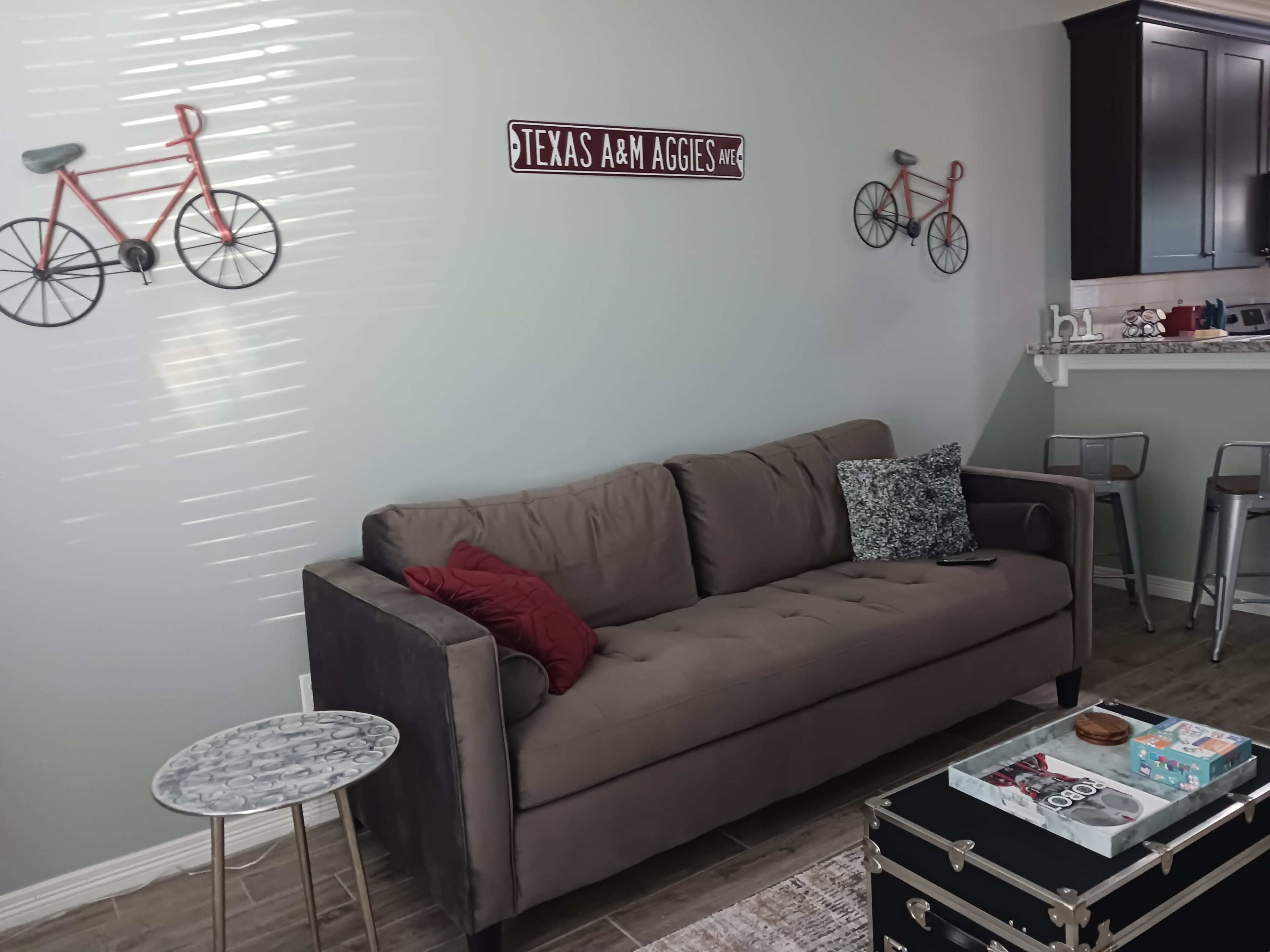 The image shows a cozy living room with a brown sofa, decorative bicycles on the wall, and a small round table next to it.