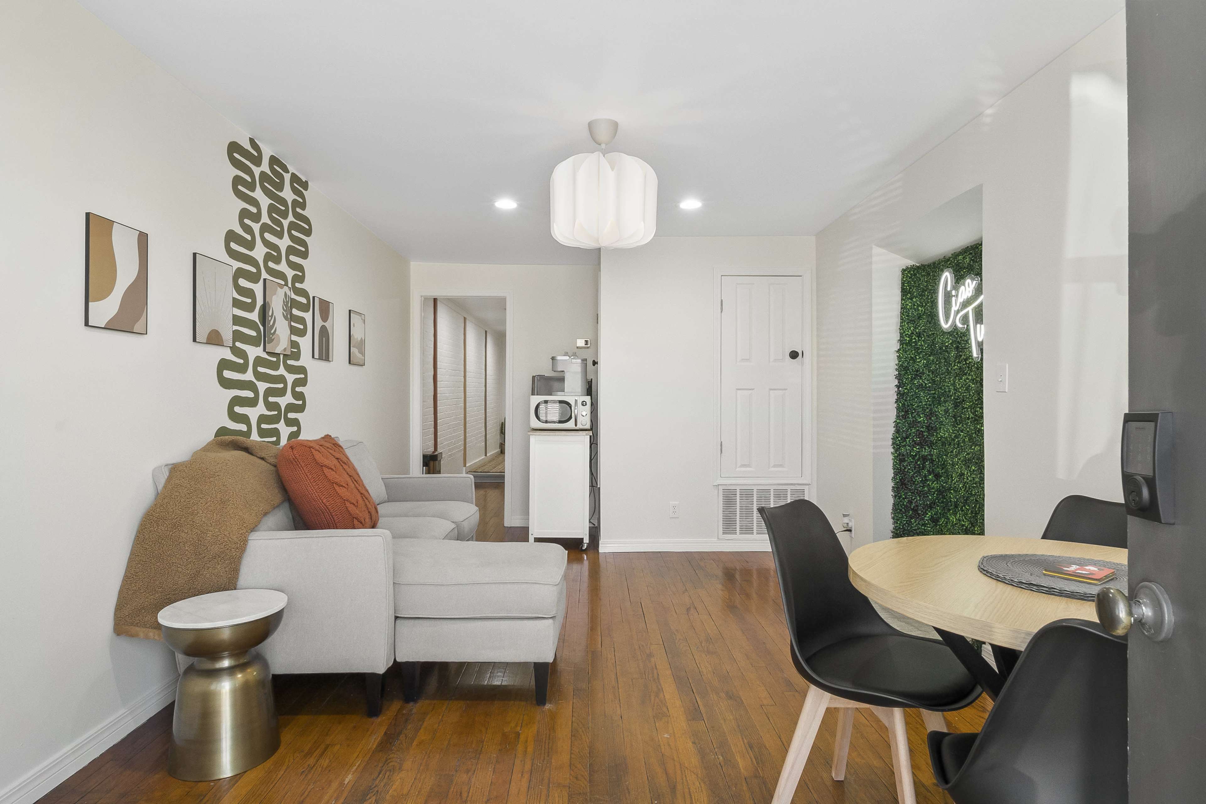 The image shows a modern living area with a sofa, a round dining table, and a kitchenette featuring a microwave and a decorative green wall.