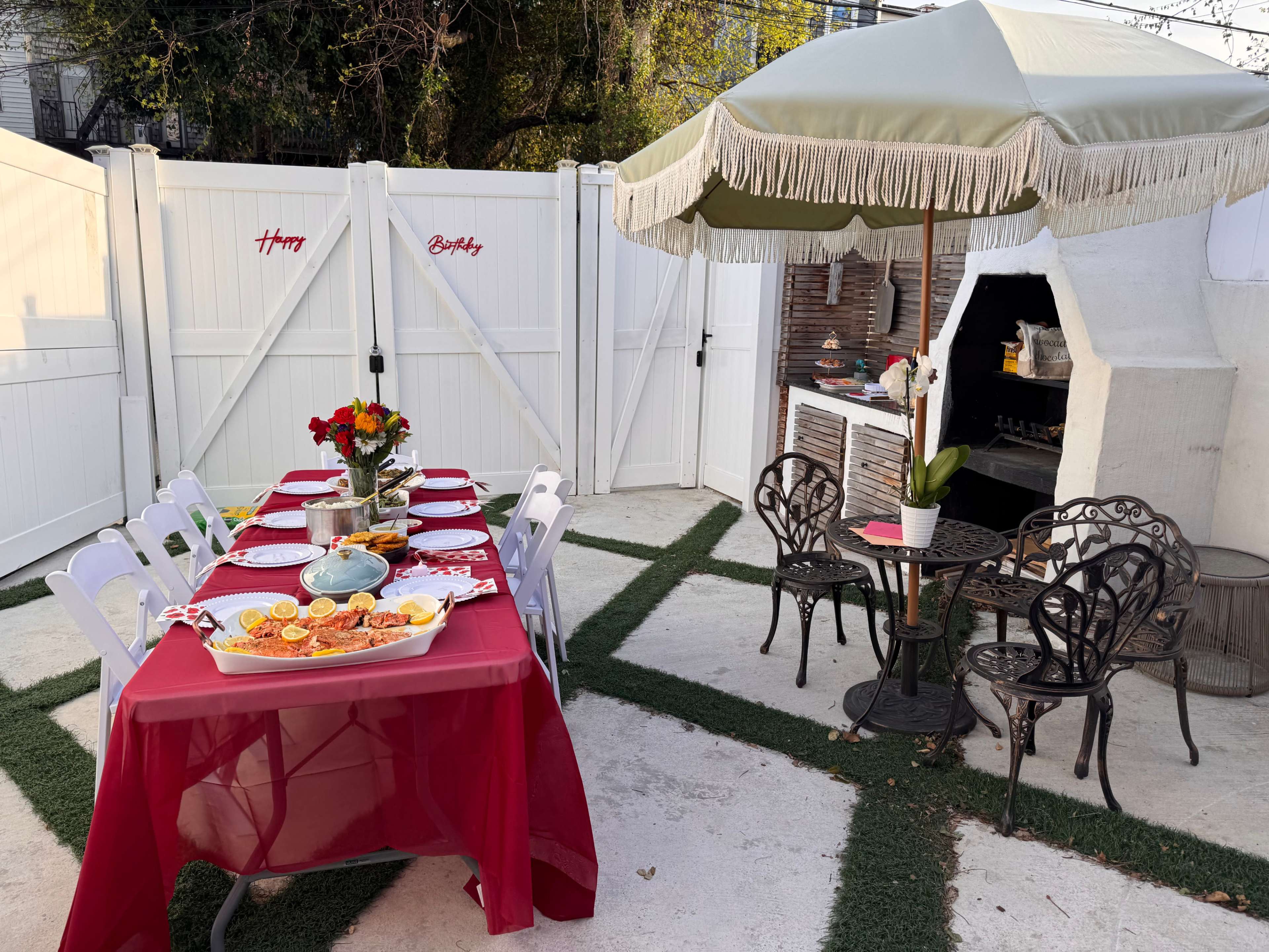 A table is set with red tablecloths and plates for a birthday celebration, surrounded by a small patio area with an outdoor grill and seating.