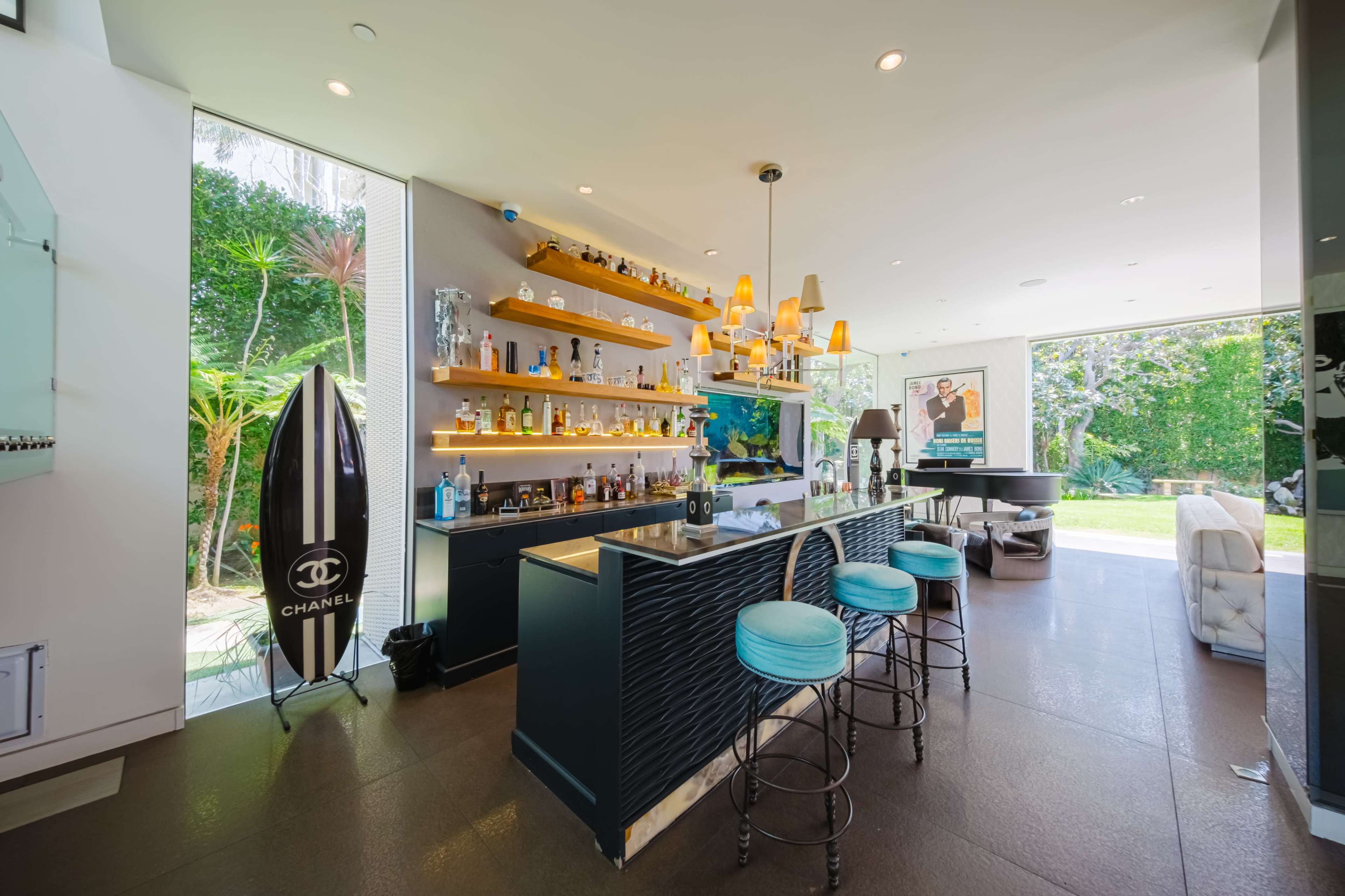 A modern bar area with a sleek countertop, shelves displaying various bottles, and a large window overlooking a garden.