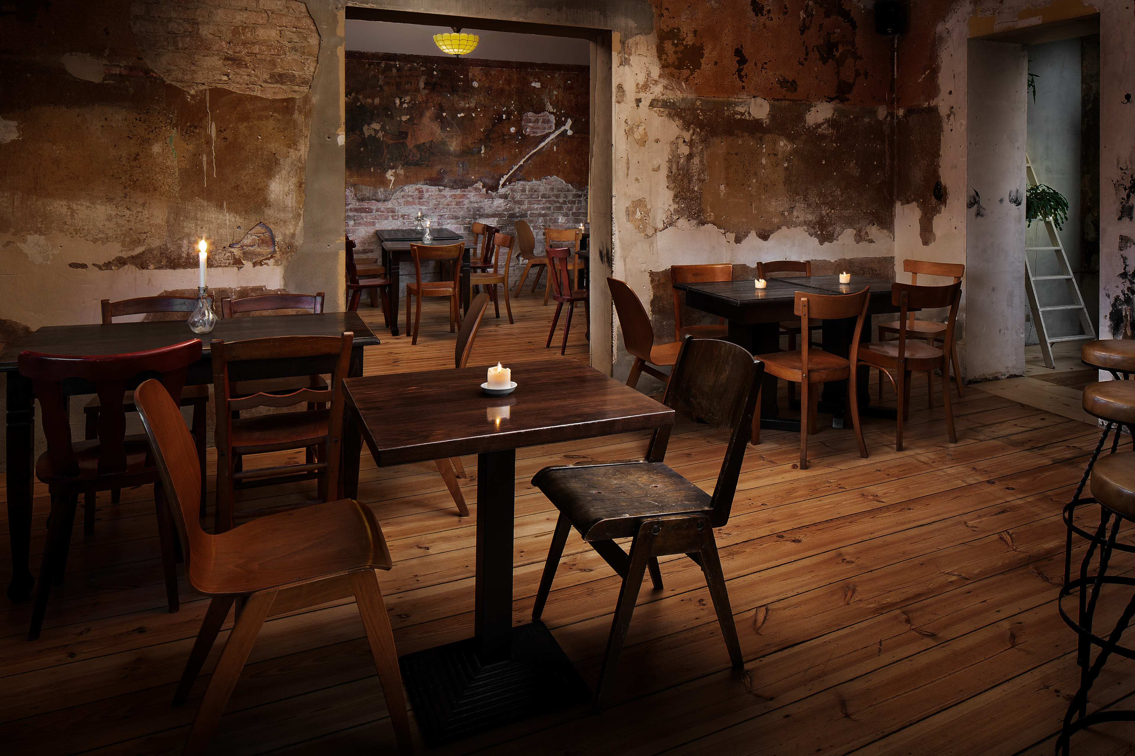 A rustic interior of a casual dining space with wooden tables and chairs arranged around a dimly lit room featuring exposed brick and peeling walls.