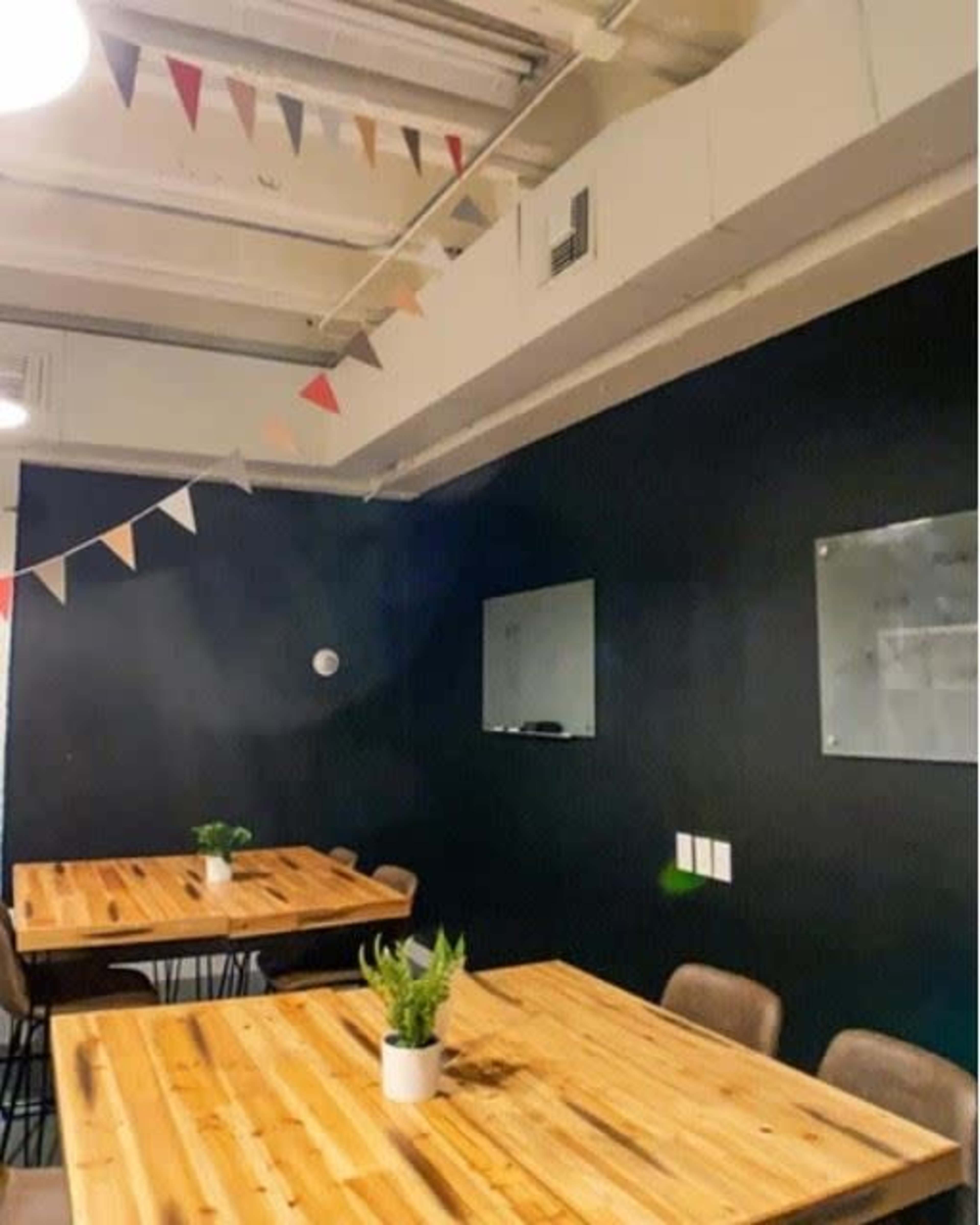 A meeting room with two wooden tables, small plants as centerpieces, and colorful triangular flags hanging from the ceiling.