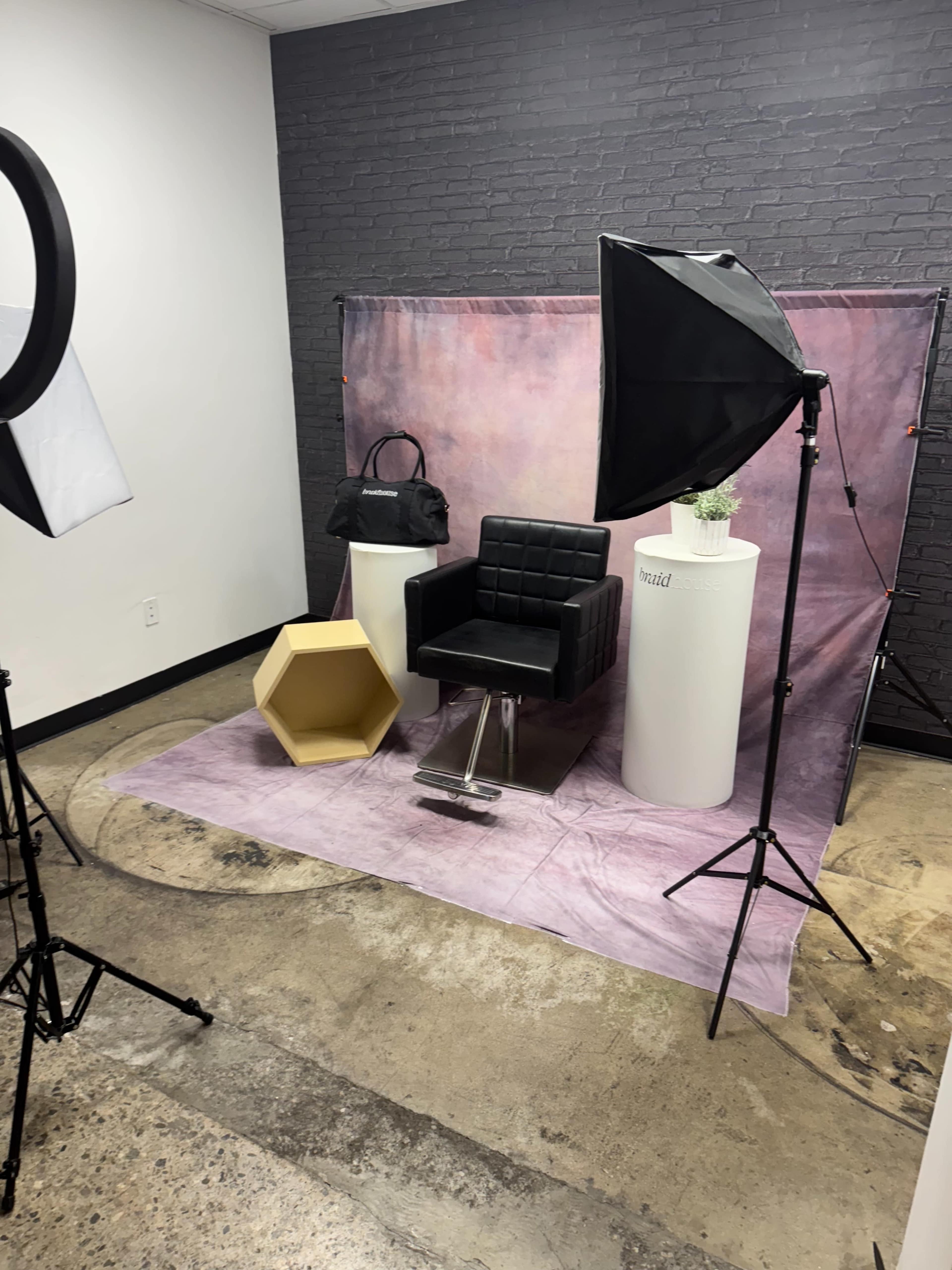 The image shows a photography setup featuring a black chair, a hexagonal yellow display, and two light sources against a textured backdrop.