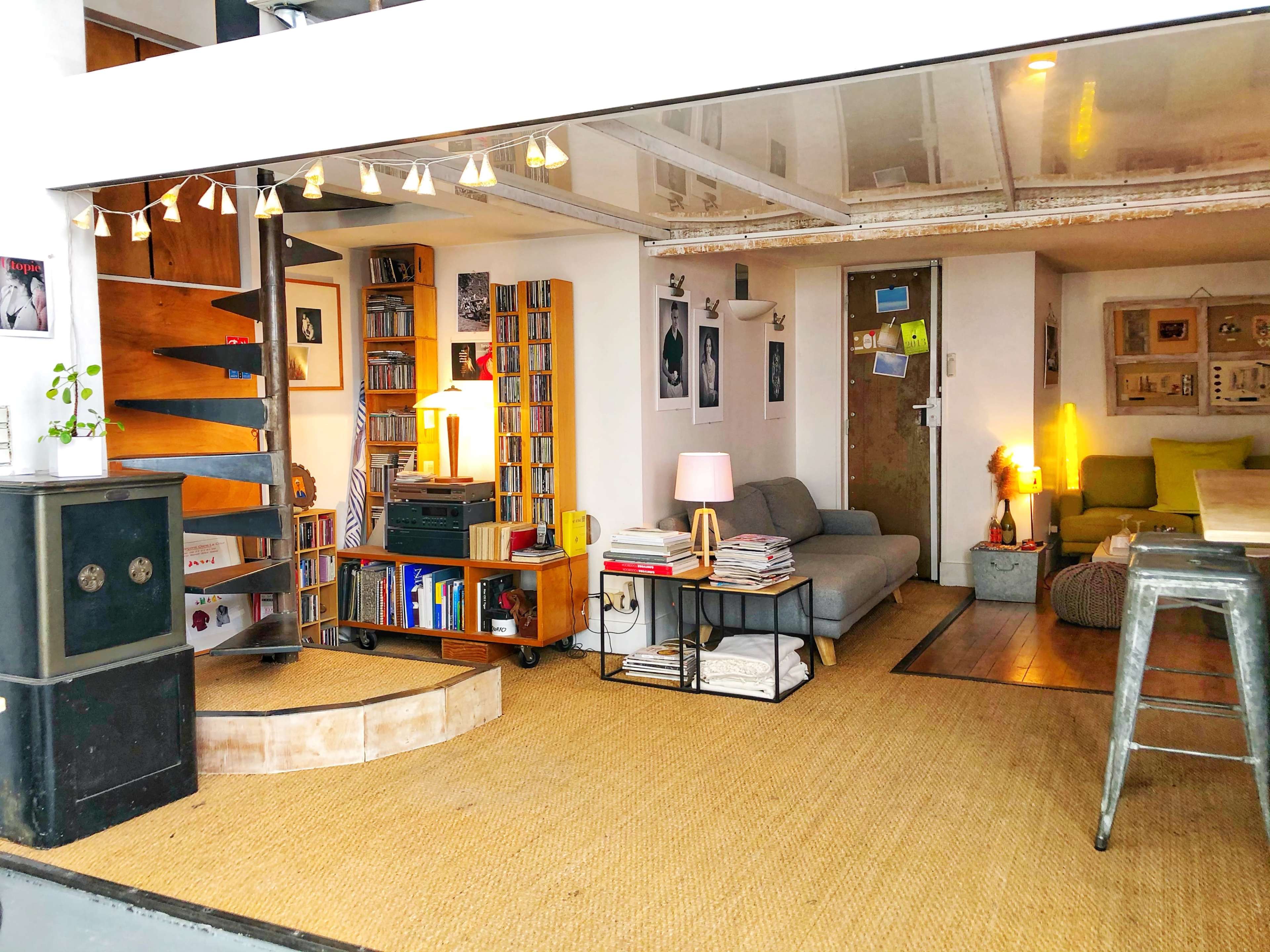 The image shows a modern living space featuring a sofa, bookshelves, a coffee table, and a warm light fixture, with a mix of textures and colors throughout the room.