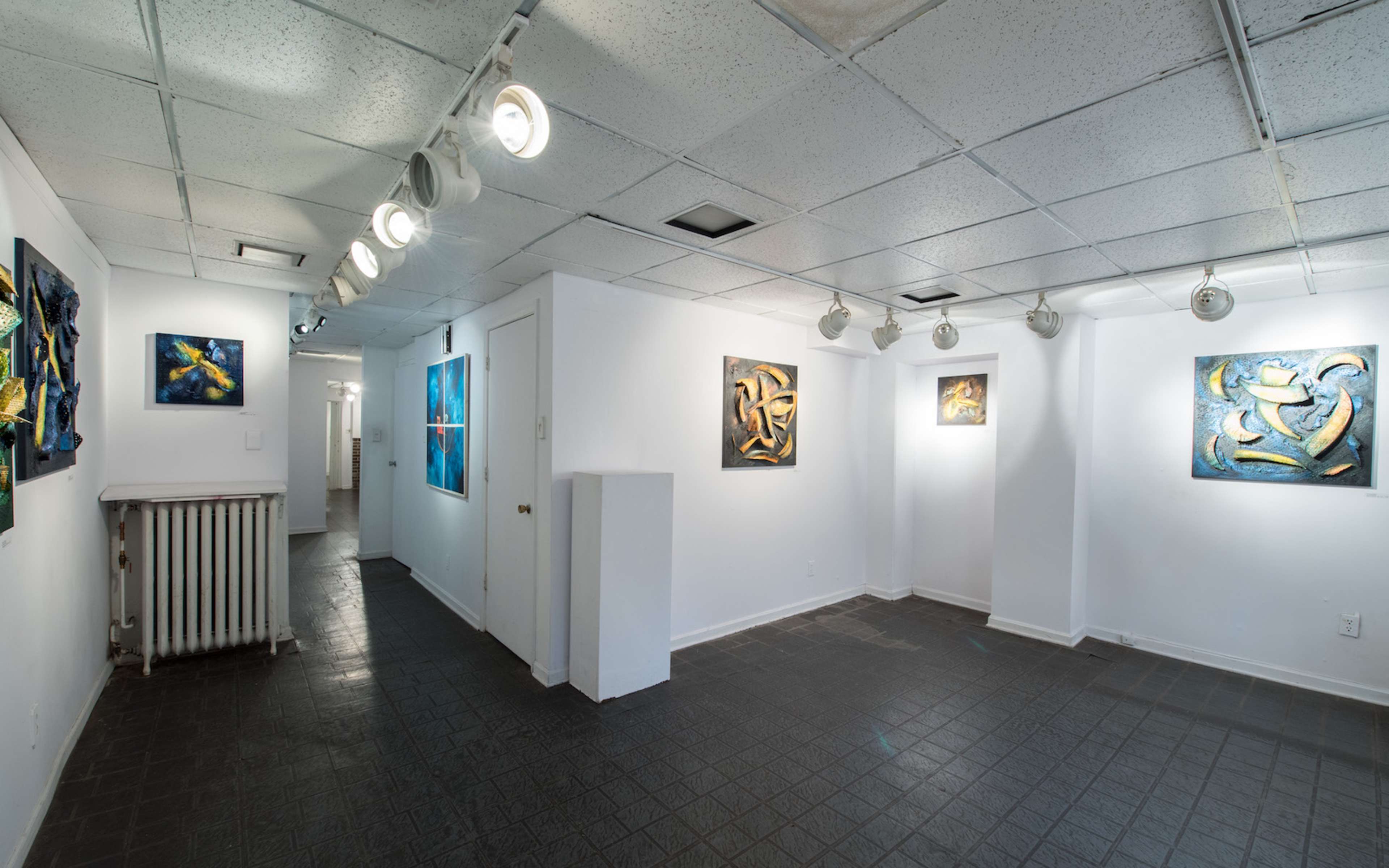 A spacious art gallery featuring several abstract paintings on white walls and a dark tiled floor.