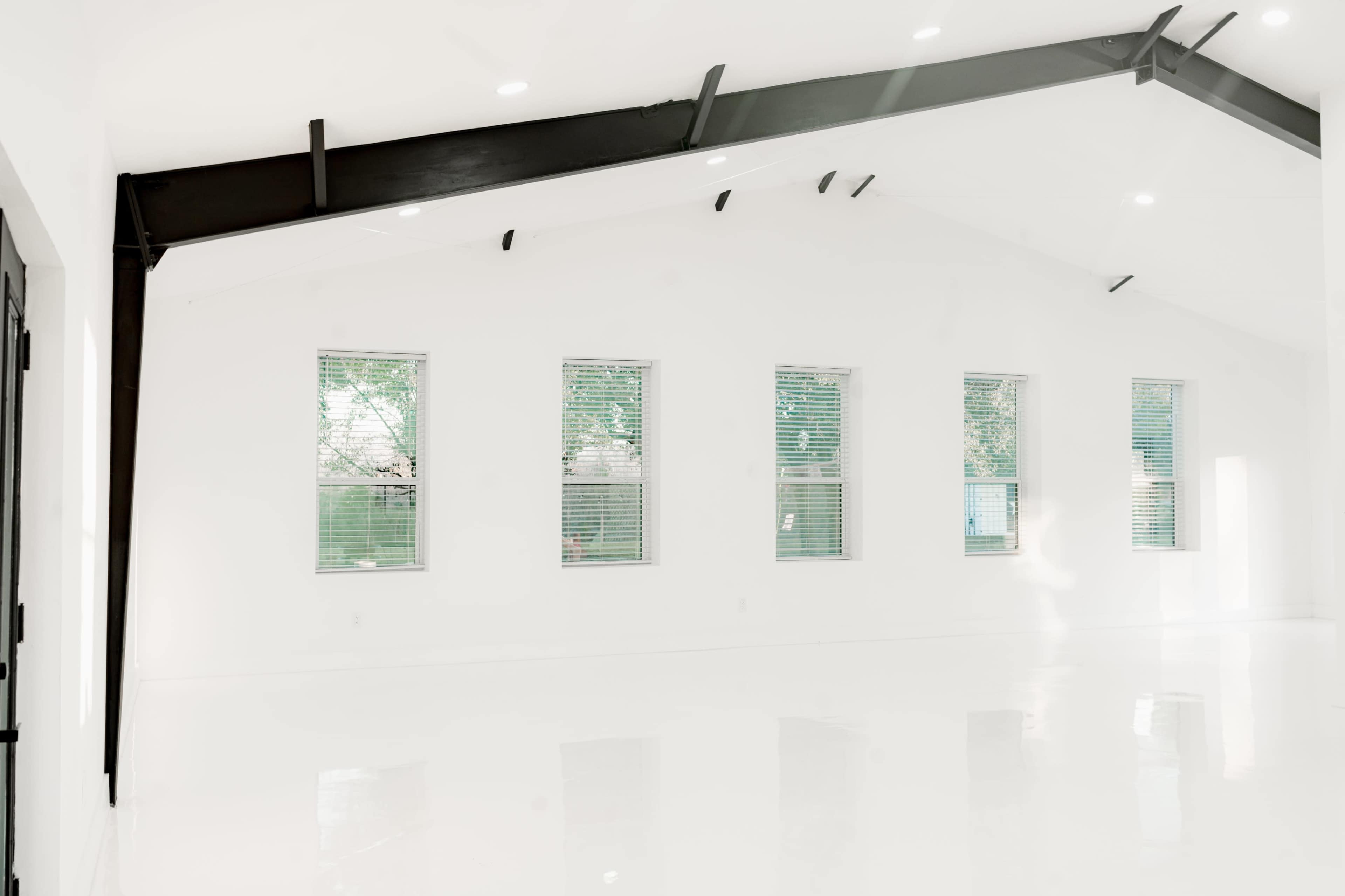 The image shows a modern, empty room with white walls, glossy floors, and large windows on one side.
