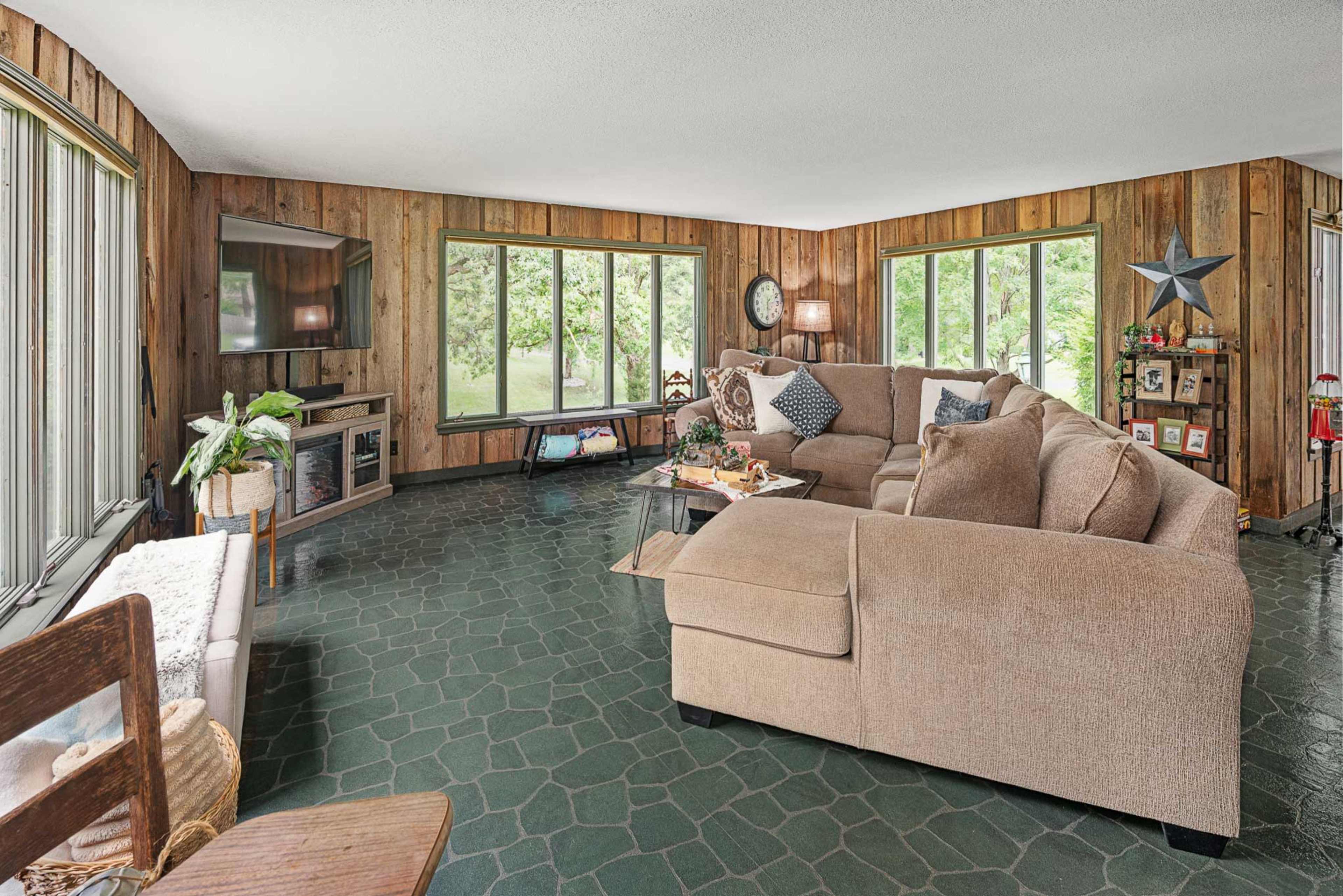 The living room features a large sectional couch, a coffee table with decorative items, and an abundance of windows that provide natural light and views of the outdoors.