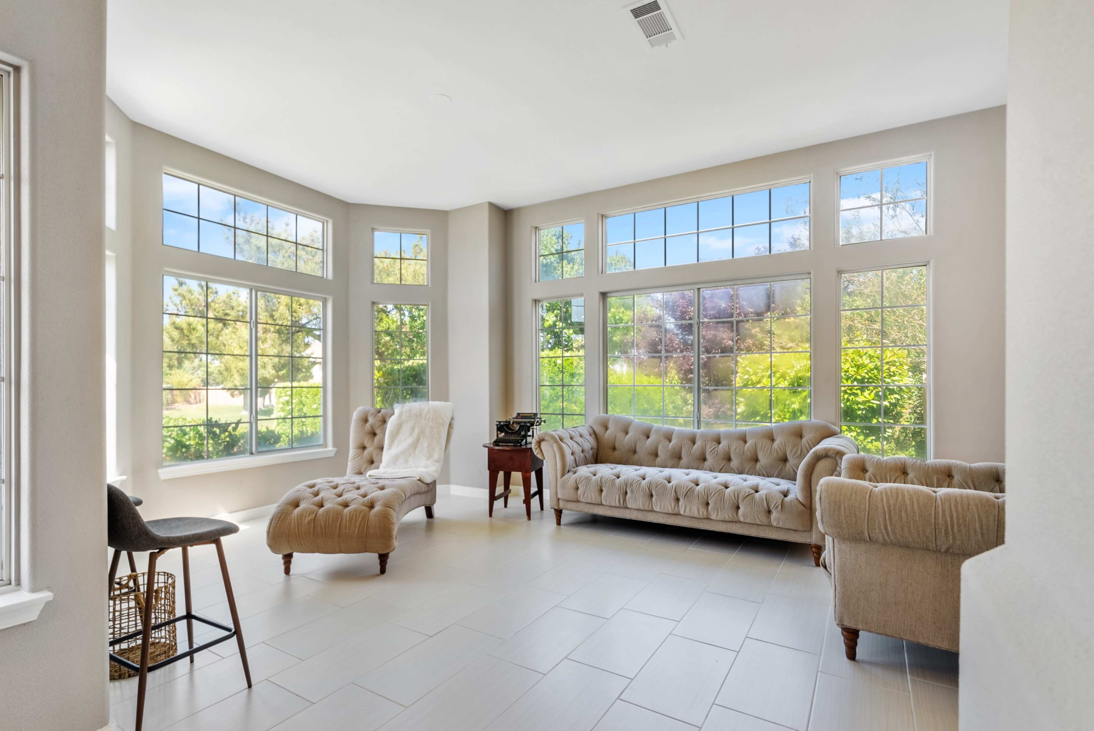 A bright room features large windows, a tufted sofa, and a small table with a typewriter.