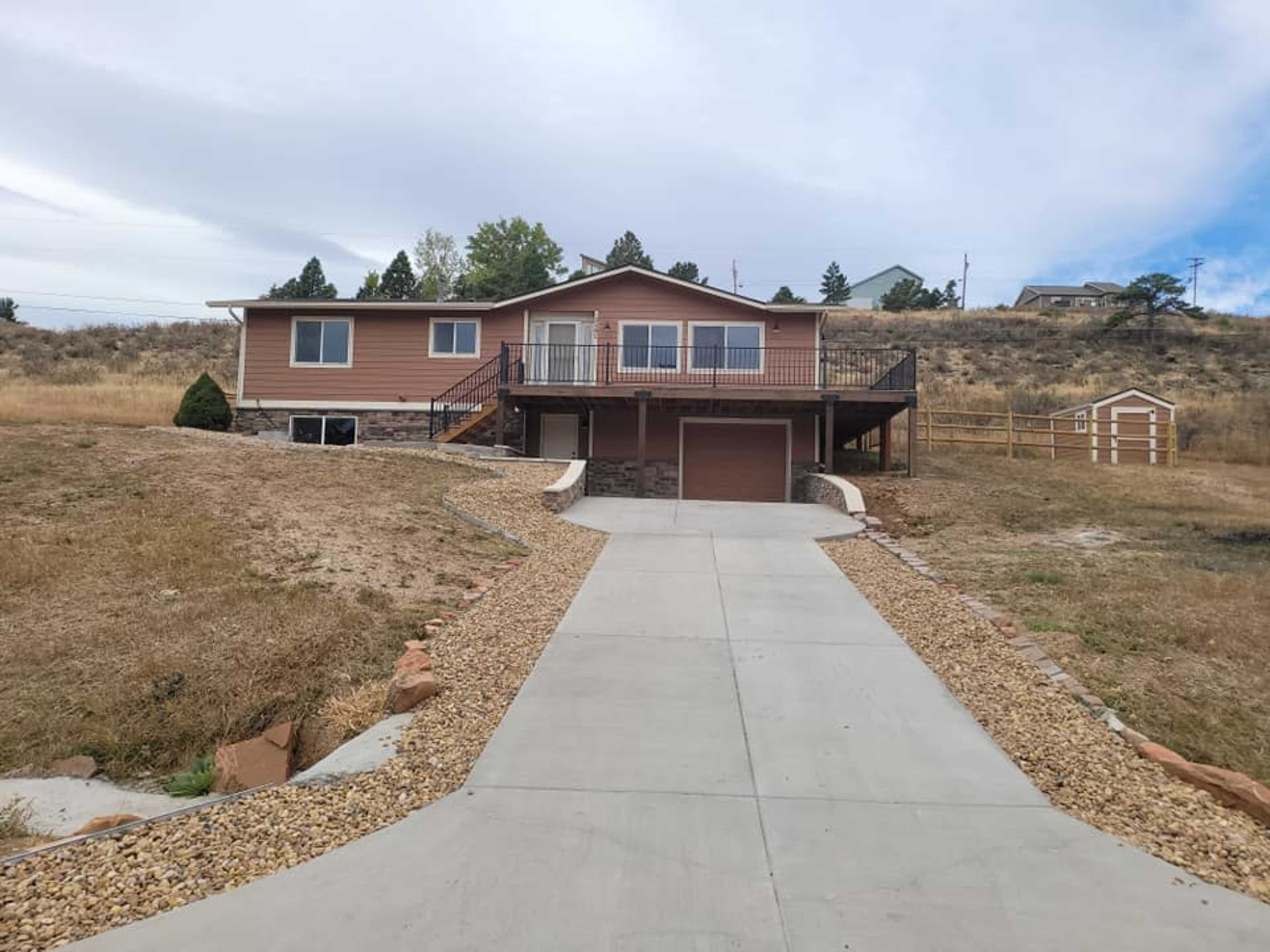 A single-story house with a driveway leading up to it, surrounded by dry grass and a few trees in the background.
