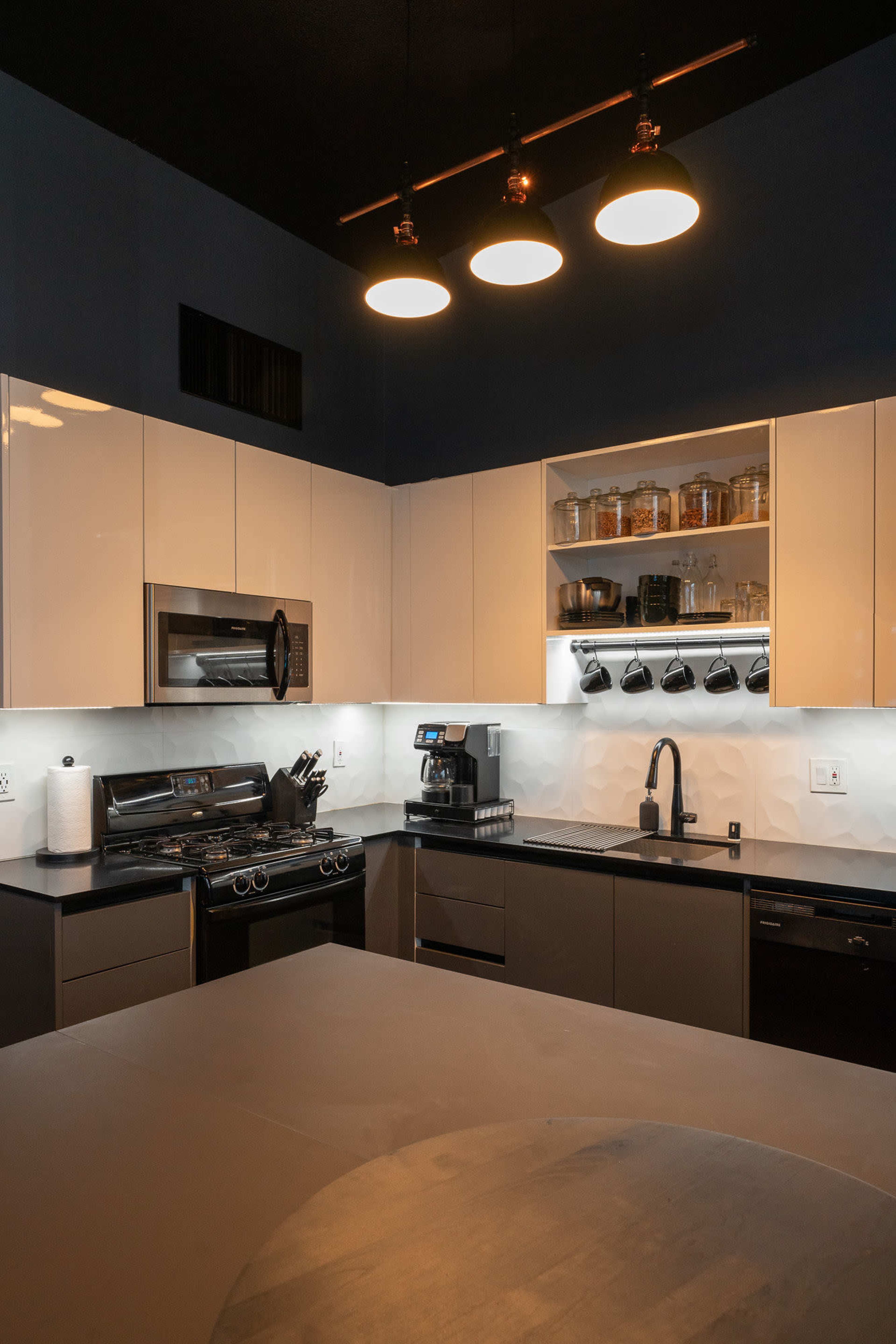 A modern kitchen features sleek cabinetry, stainless steel appliances, and a central island with a circular top, illuminated by pendant lights.