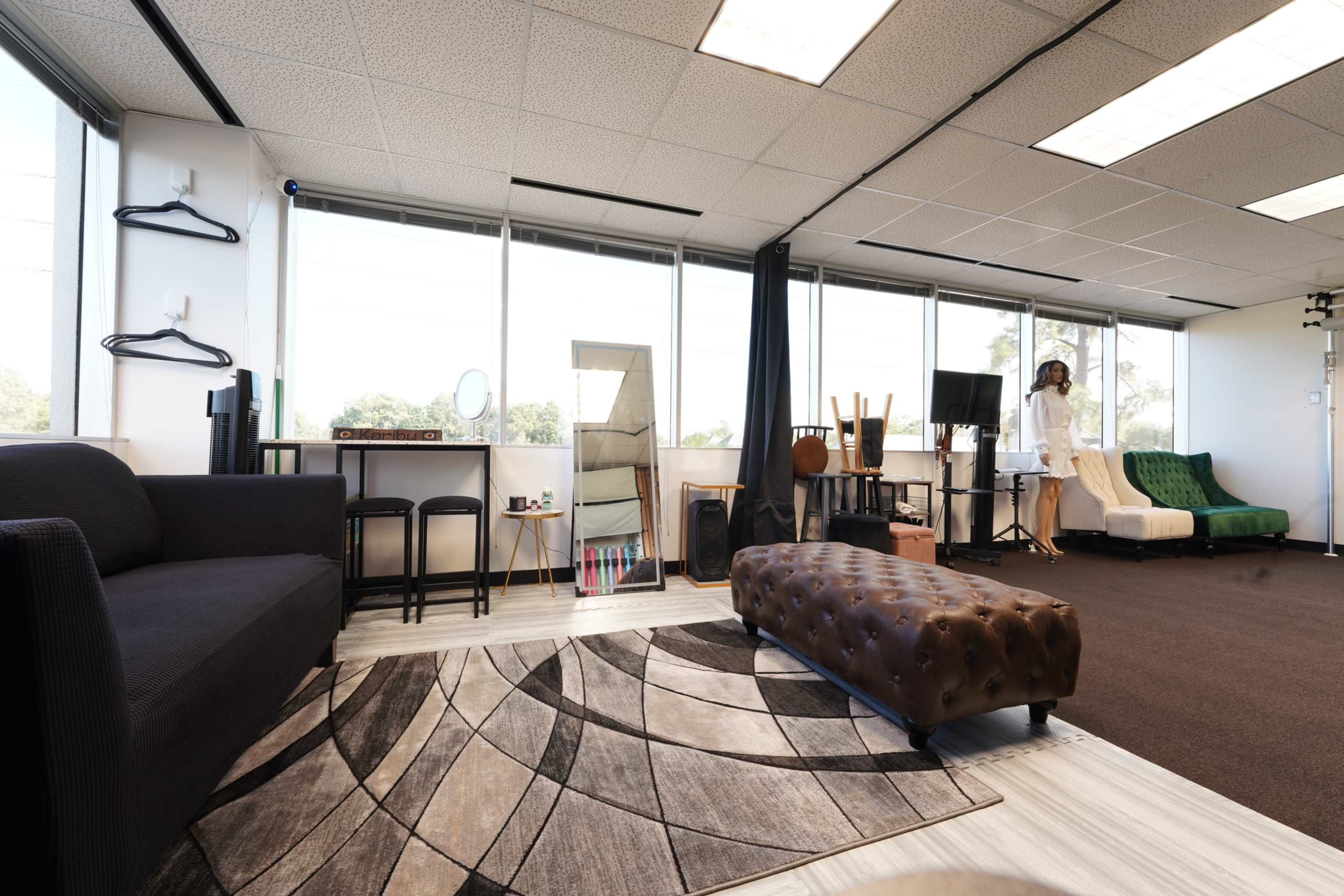 A modern studio space with a couch, bar stools, a rug, a large mirror, and various musical instruments arranged near a window.
