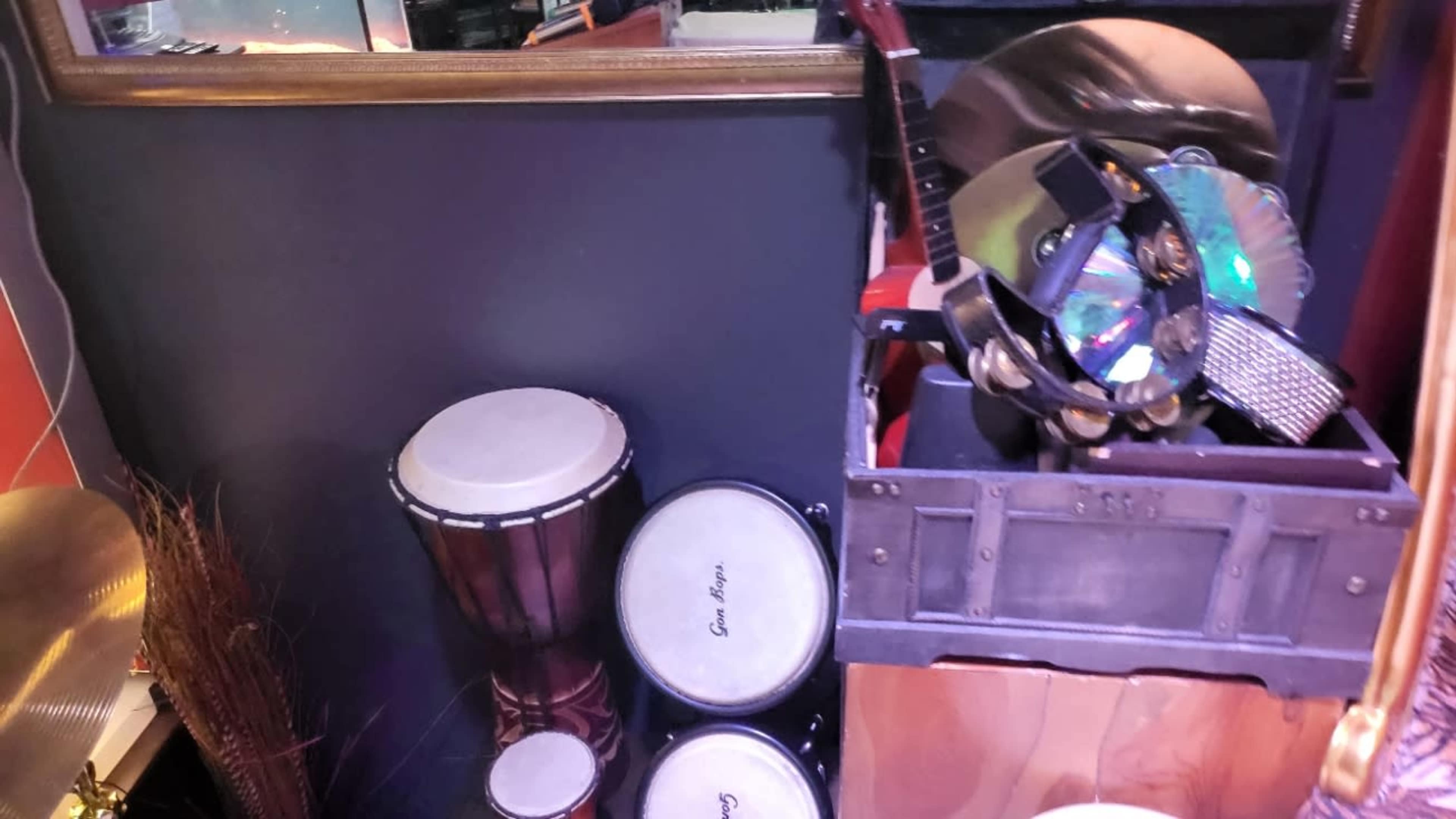 A collection of musical instruments, including drums and a guitar, arranged near a mirrored wall with decorative elements.