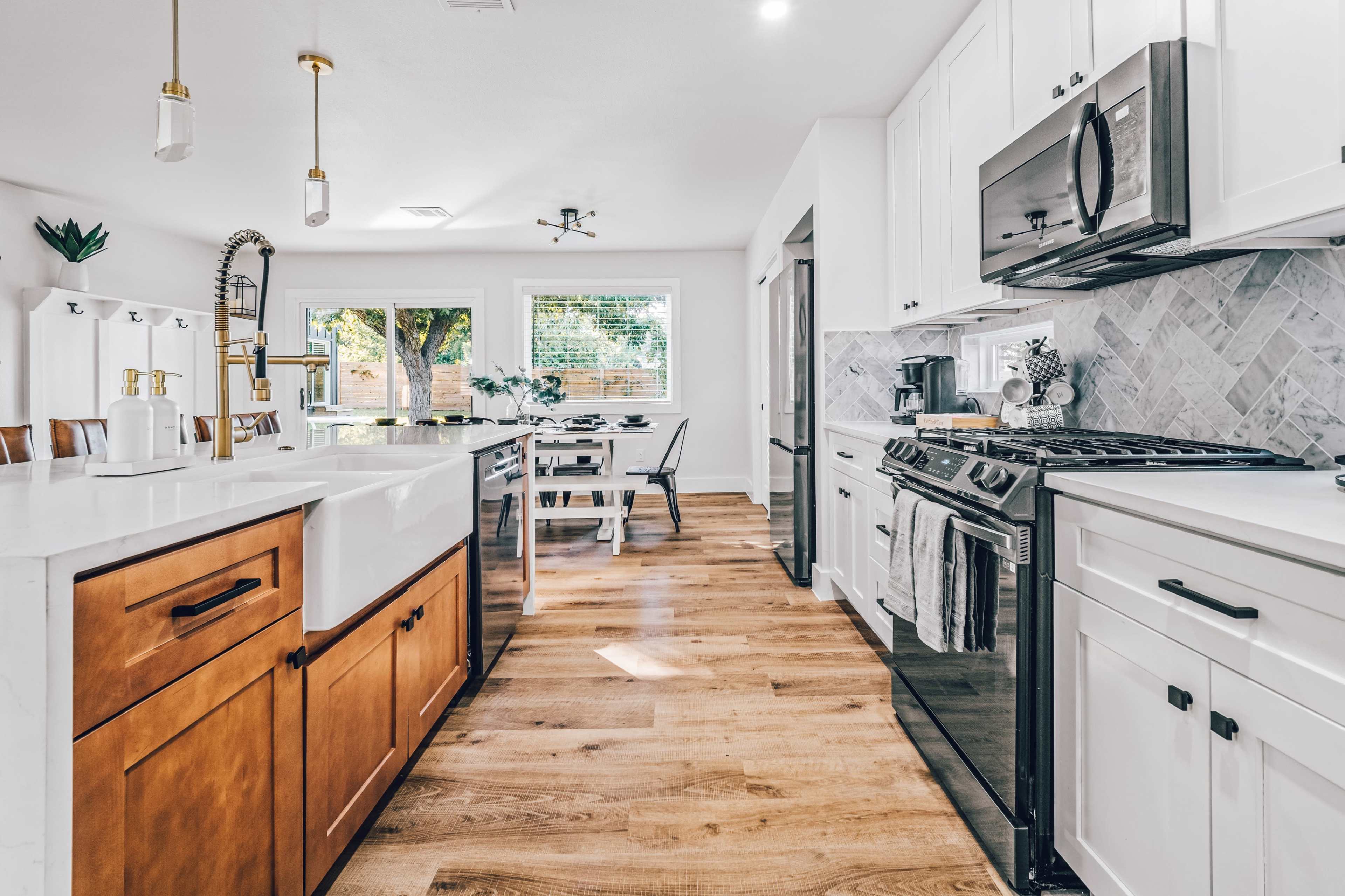A modern kitchen with a central island, wooden cabinets, stainless steel appliances, and a dining area visible through a window.