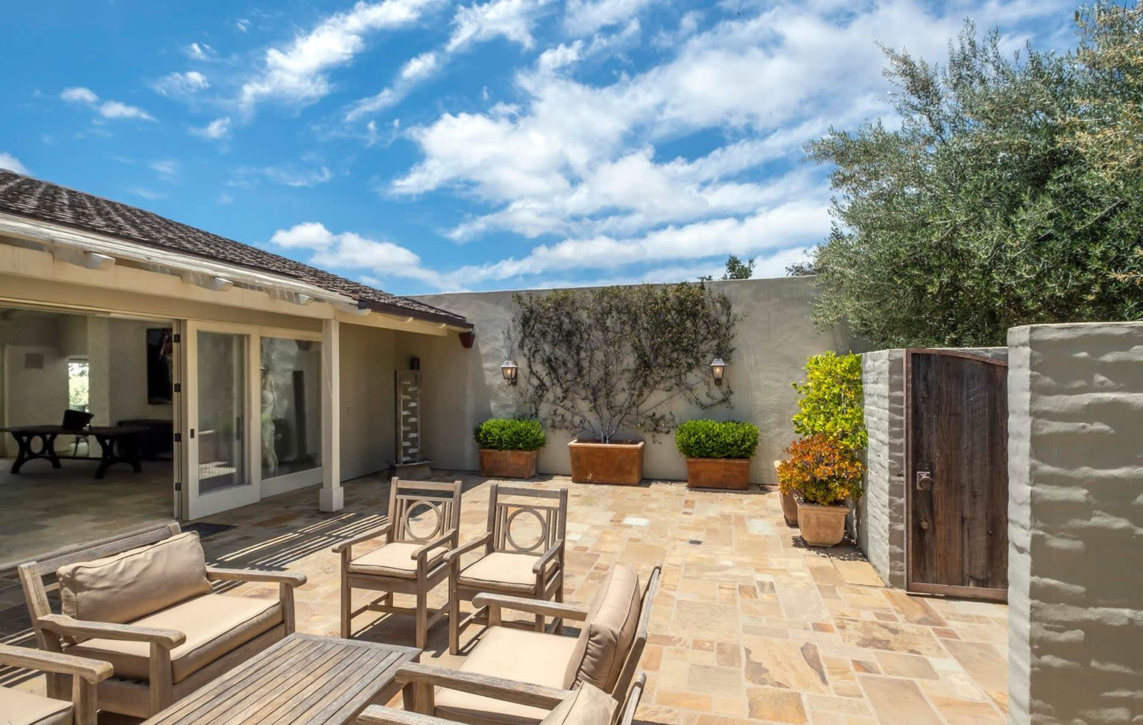 A stone patio with outdoor seating, surrounded by potted plants and a rustic wooden door.