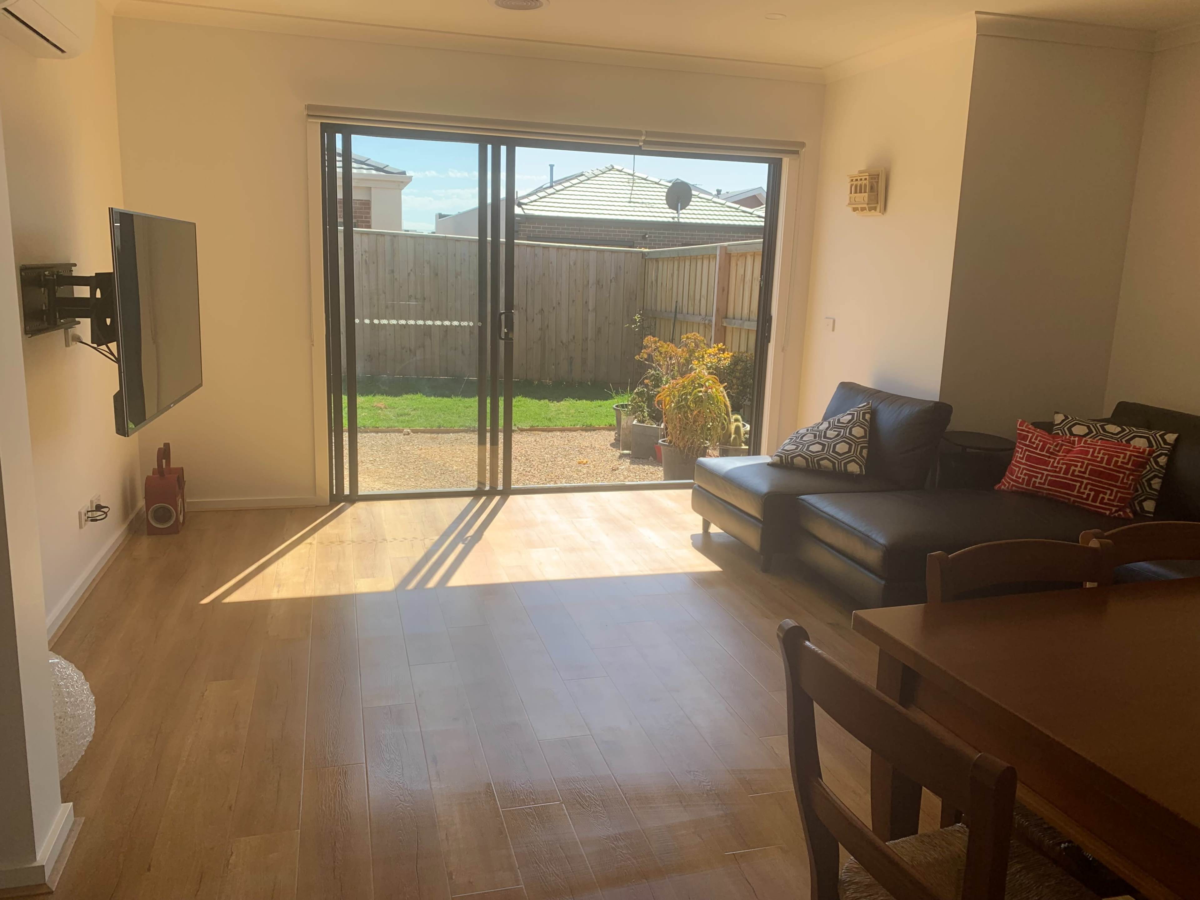 A modern living area features a black leather sofa, a wooden dining table, and large glass doors that open to a grassy outdoor space.