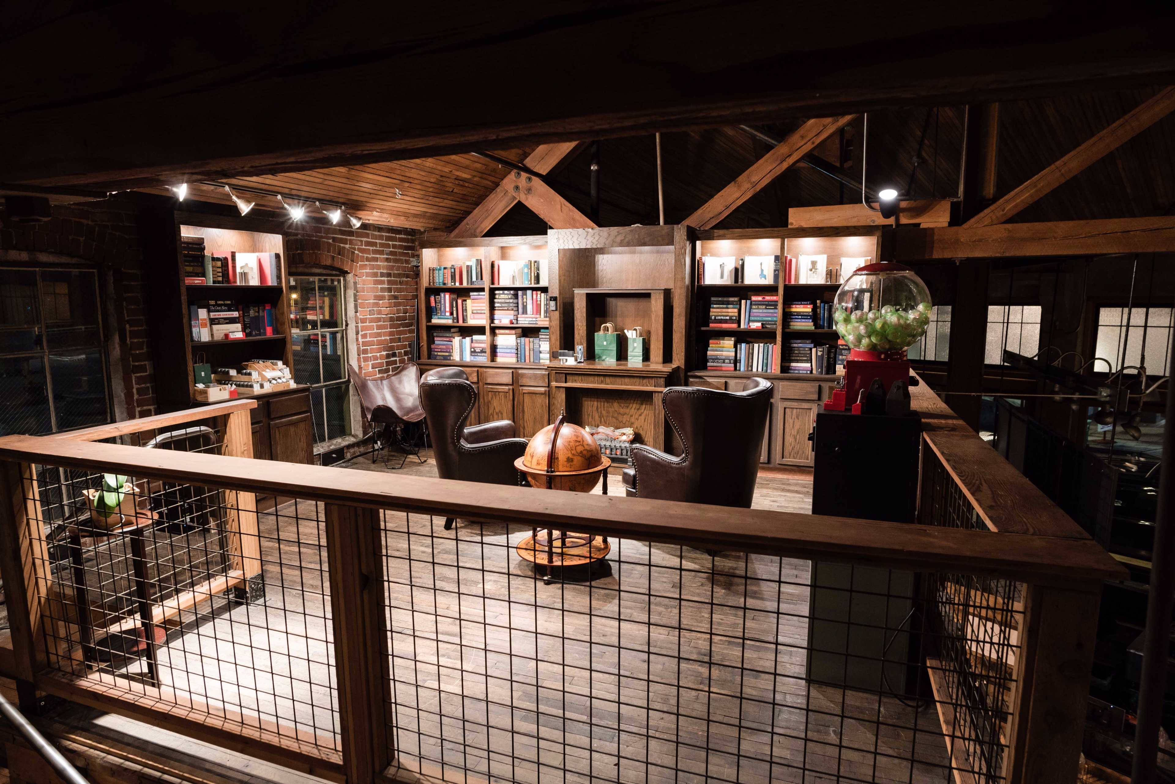 A cozy reading room features two leather chairs, a globe, and shelves filled with books, all under a wooden beamed ceiling.