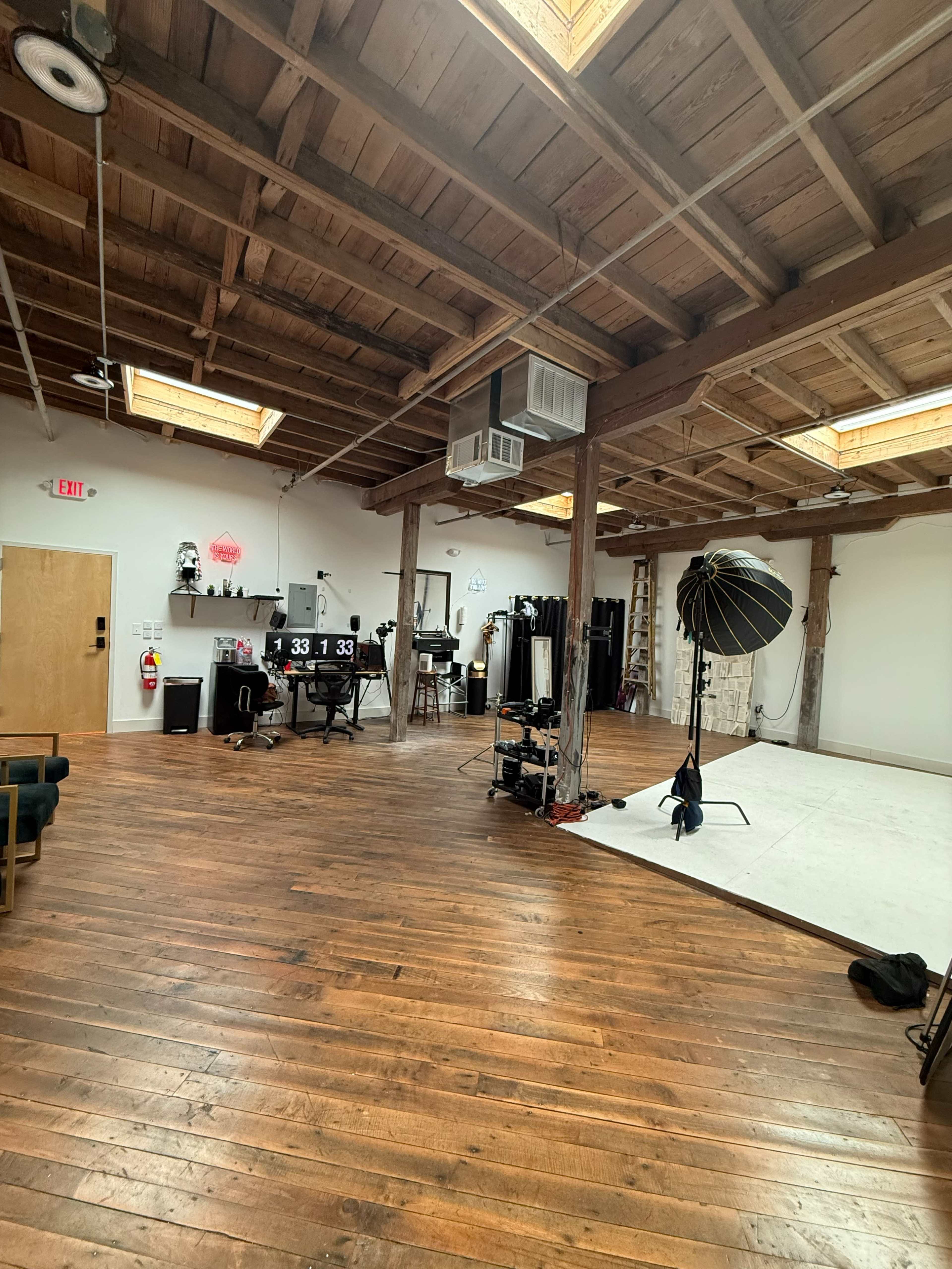 The image shows a spacious photography studio with wooden floors, skylights, and various equipment arranged around the room.