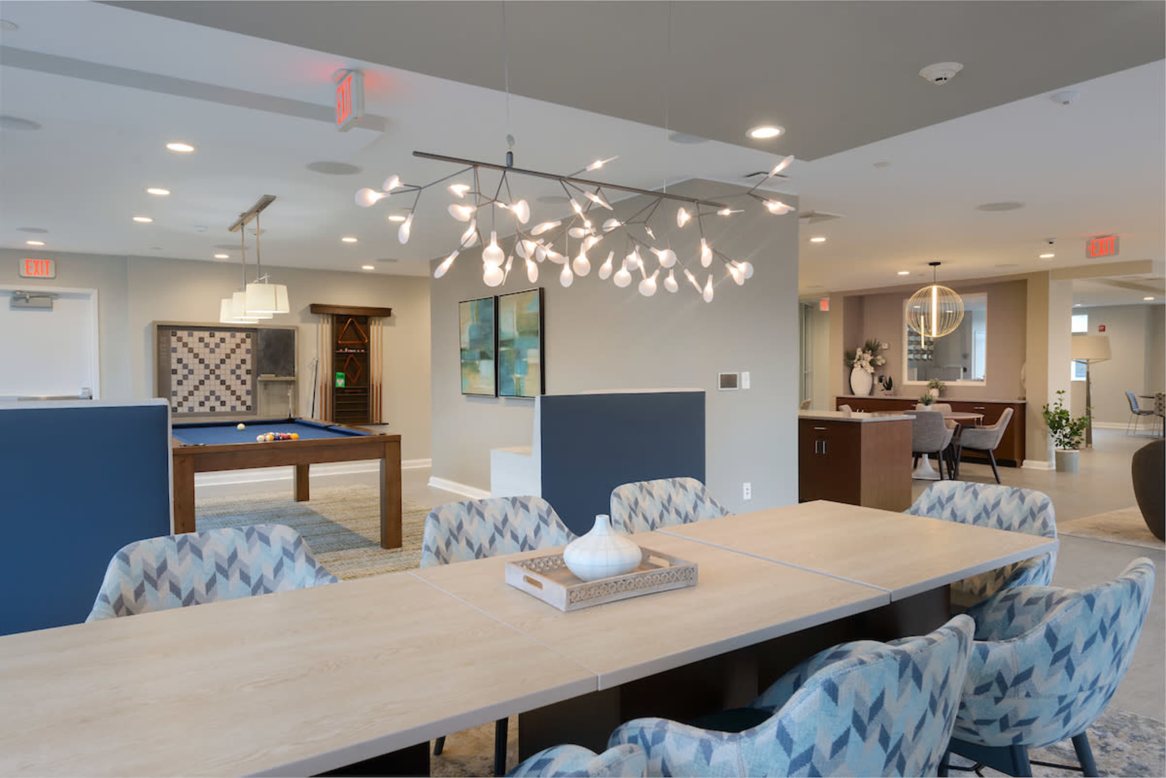 A modern communal space features a dining area with a light fixture, adjacent to a billiards table and seating areas.