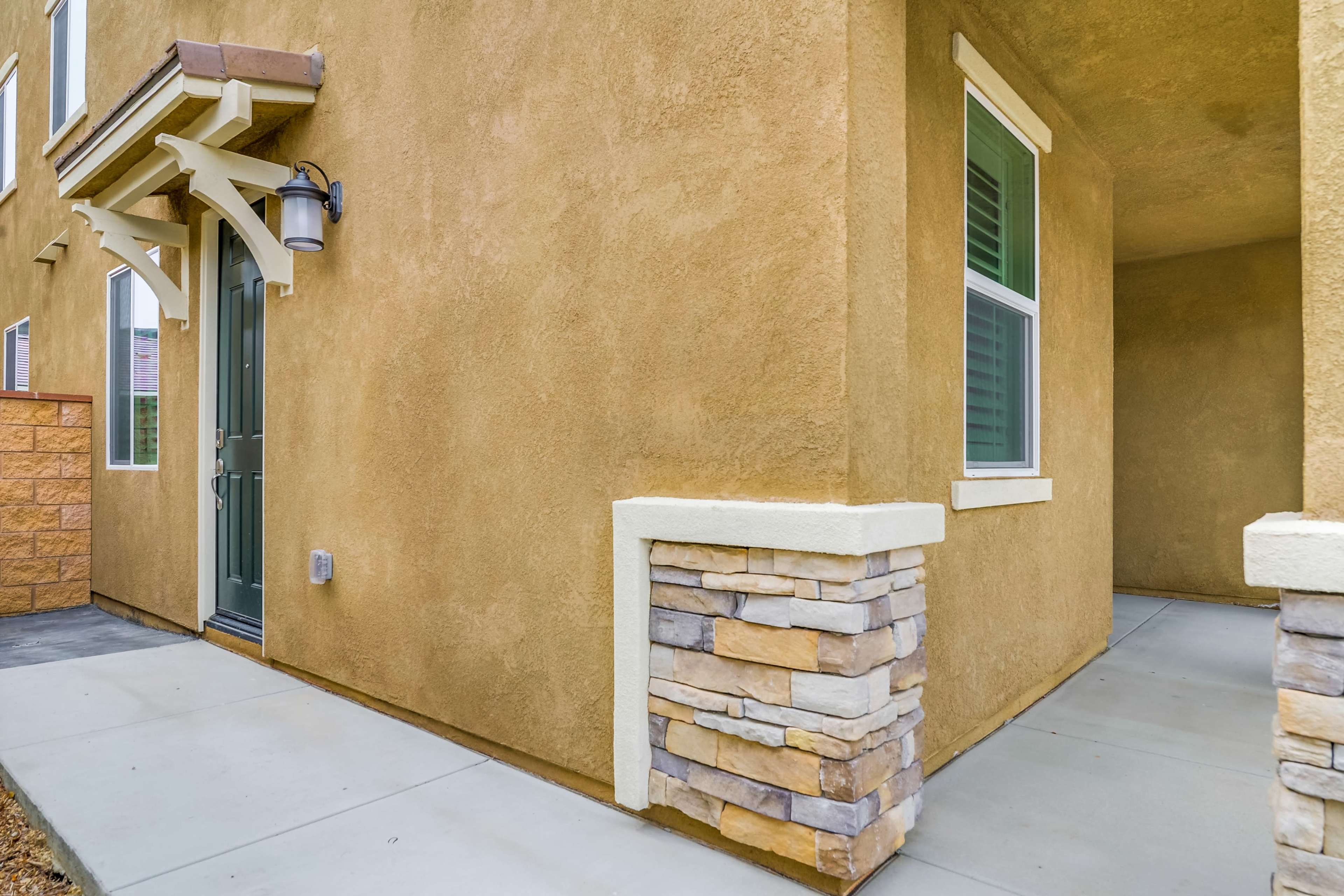 The exterior corner of a residential building with beige stucco walls, a green front door, and a stone accent wall.
