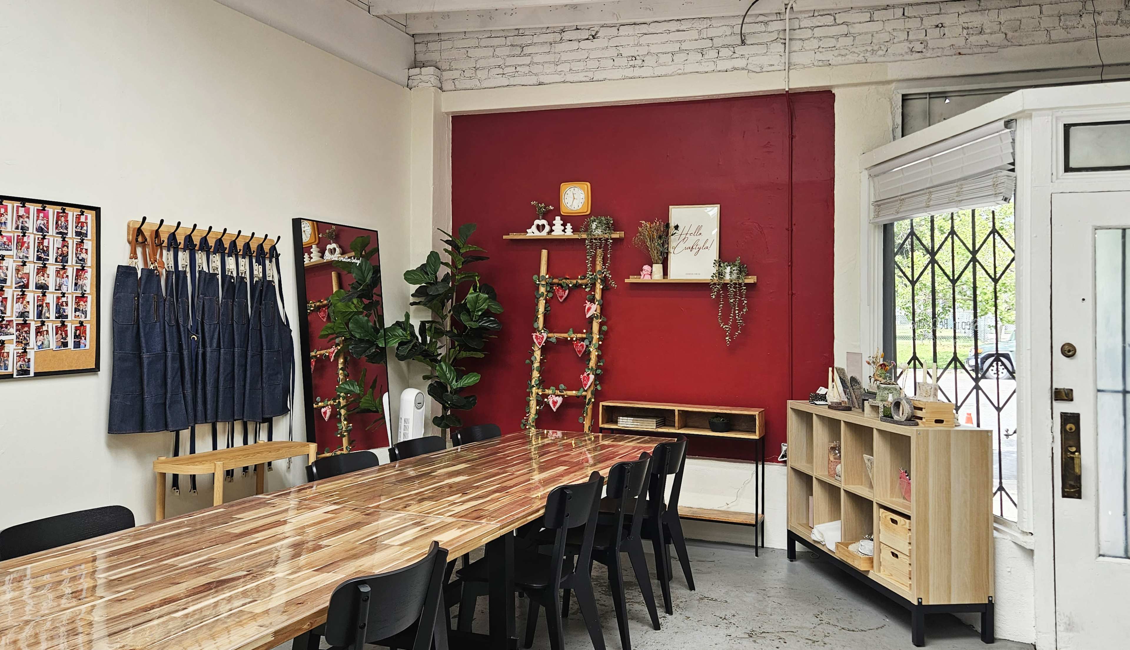 The image shows a spacious room with a long wooden table, black chairs, and red accent wall decorations, including plants and shelves.
