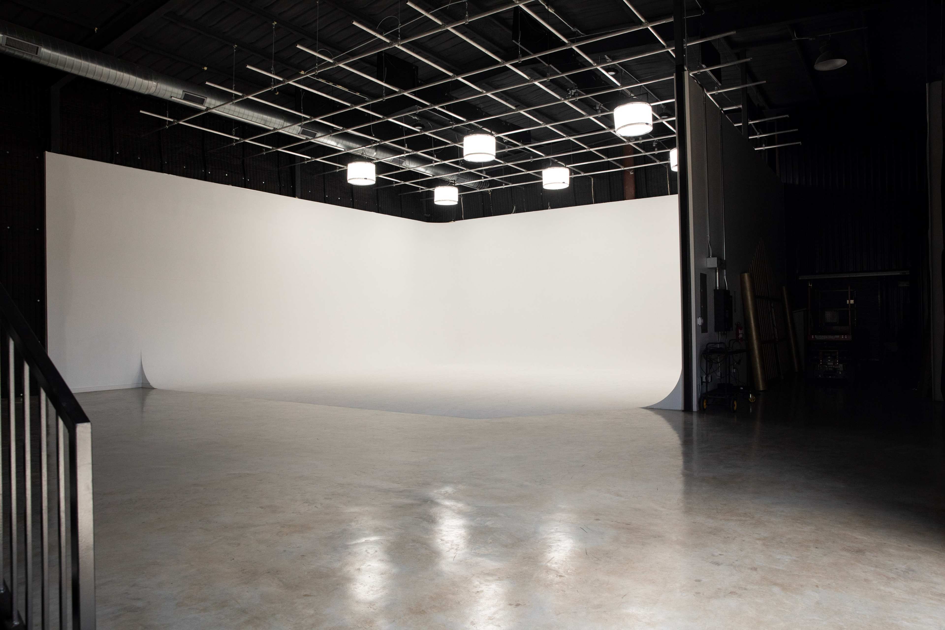 A spacious photography studio with a large white backdrop, overhead lights, and a polished concrete floor.