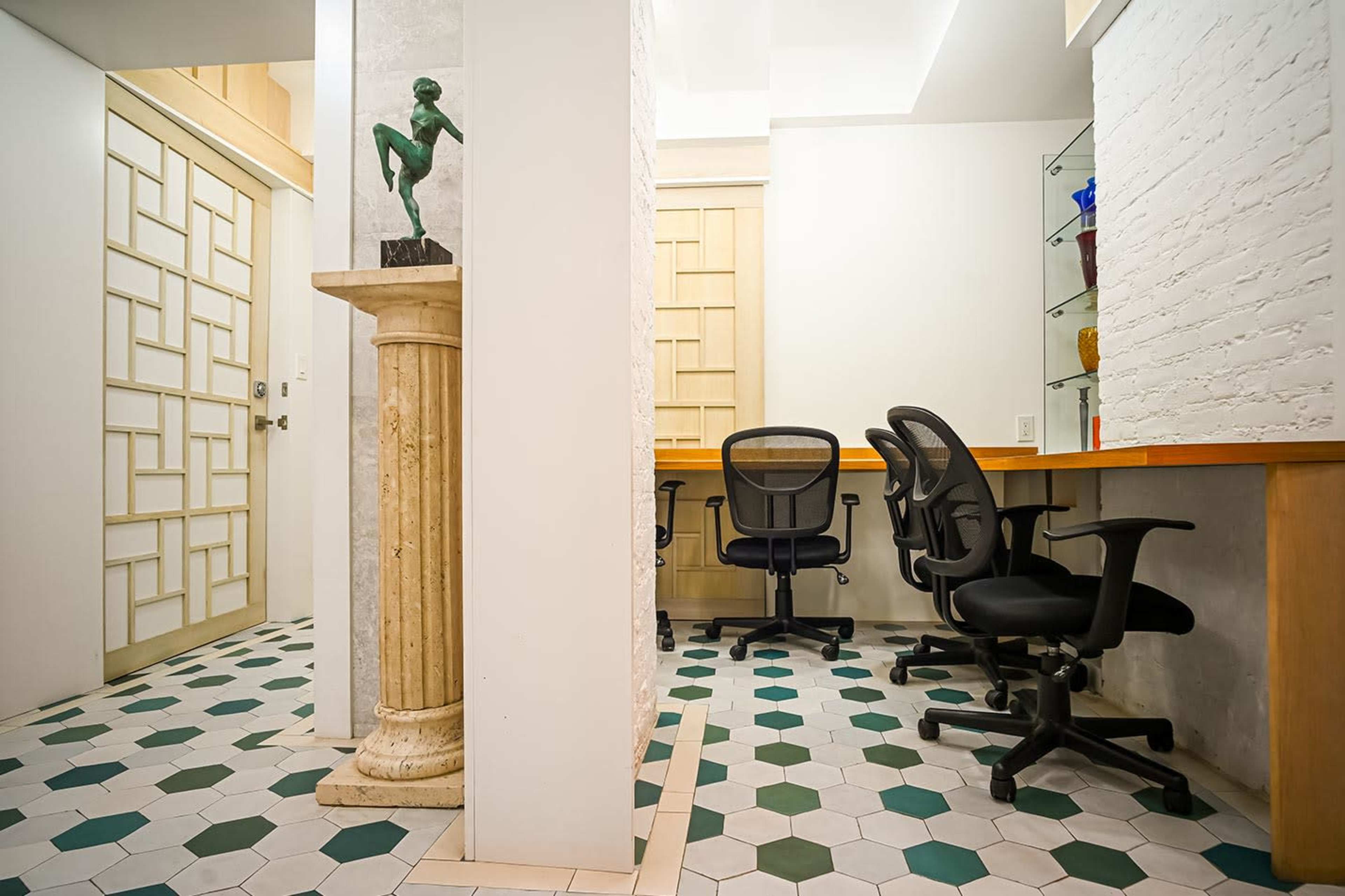 The image depicts a modern office space featuring three black office chairs, a decorative column with a statue, and a patterned hexagonal tile floor.