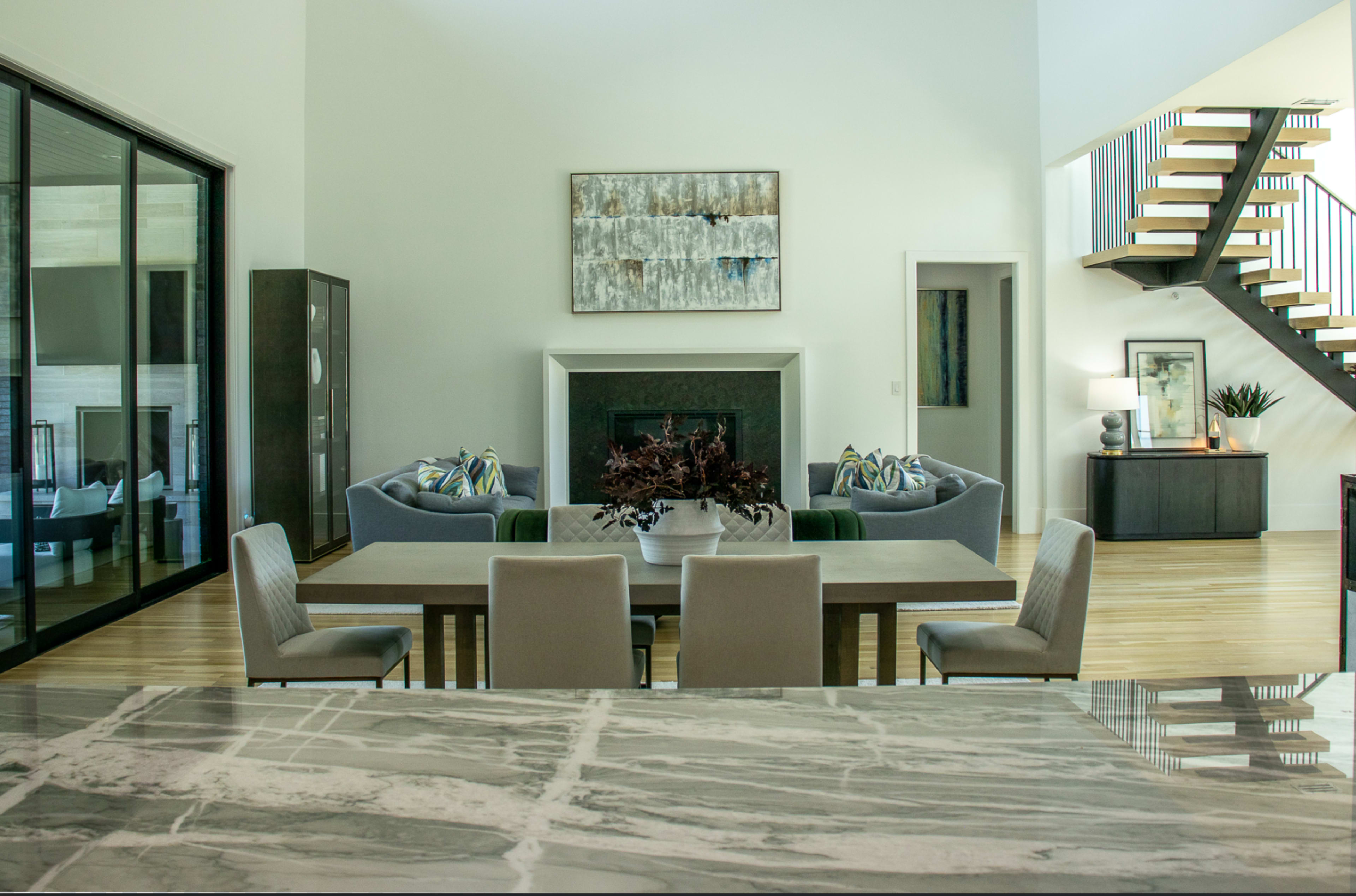 The image shows a spacious living area with a dining table, modern furniture, and a staircase in the background.