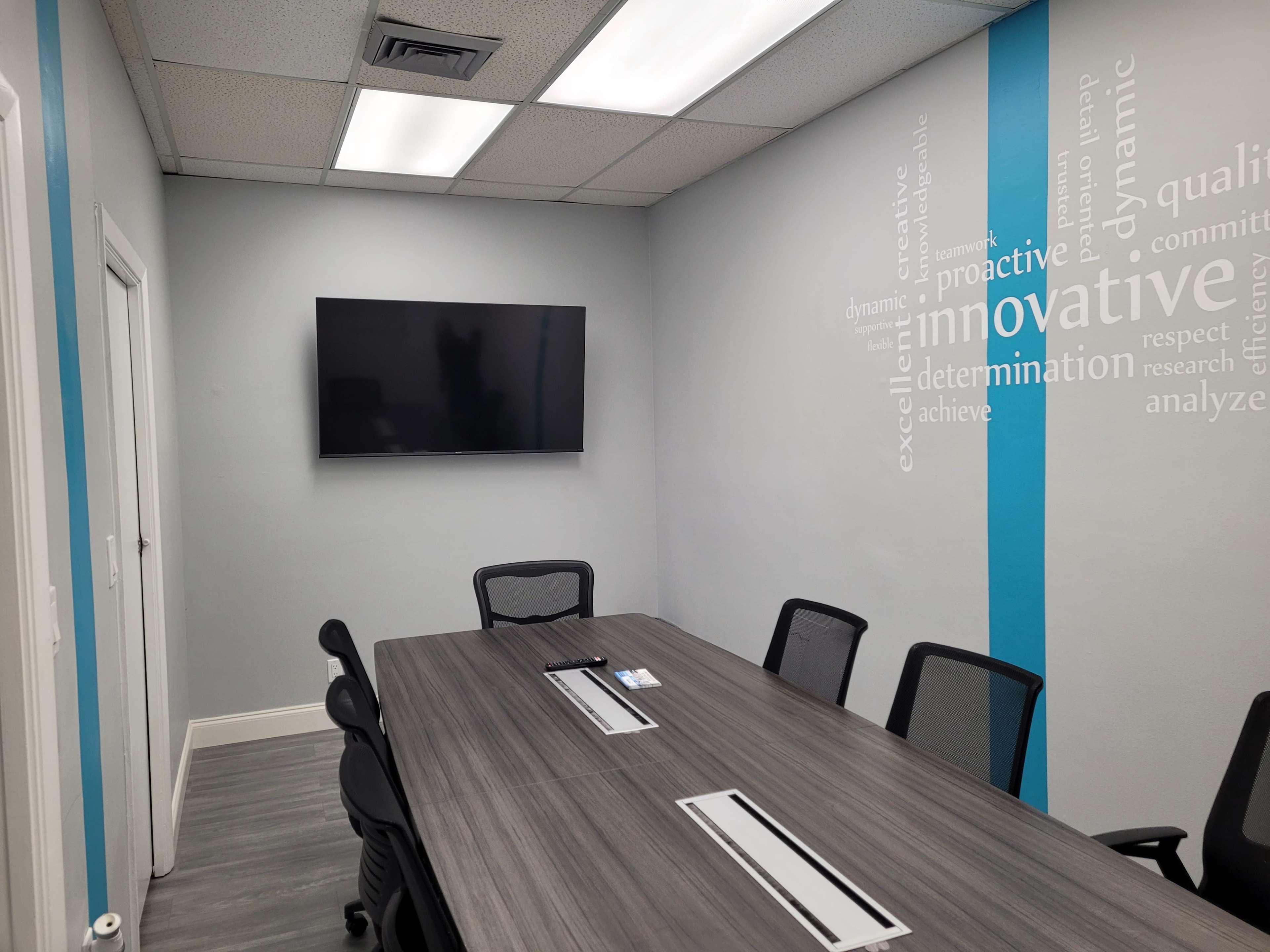 A modern conference room featuring a long wooden table, several black chairs, and a wall-mounted television.
