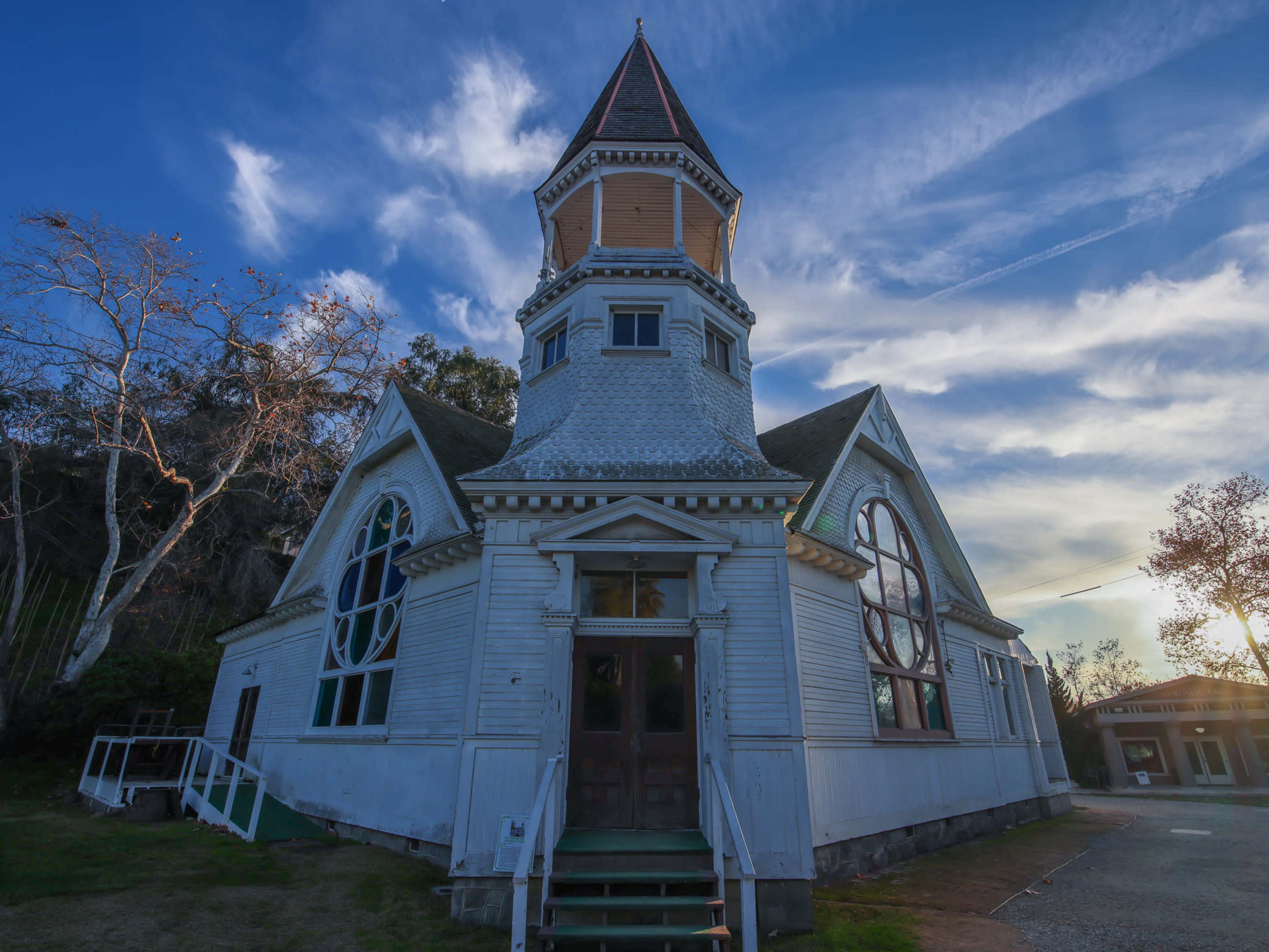 A large, historic church with a steep, pointed tower and stained-glass windows stands against a blue sky.