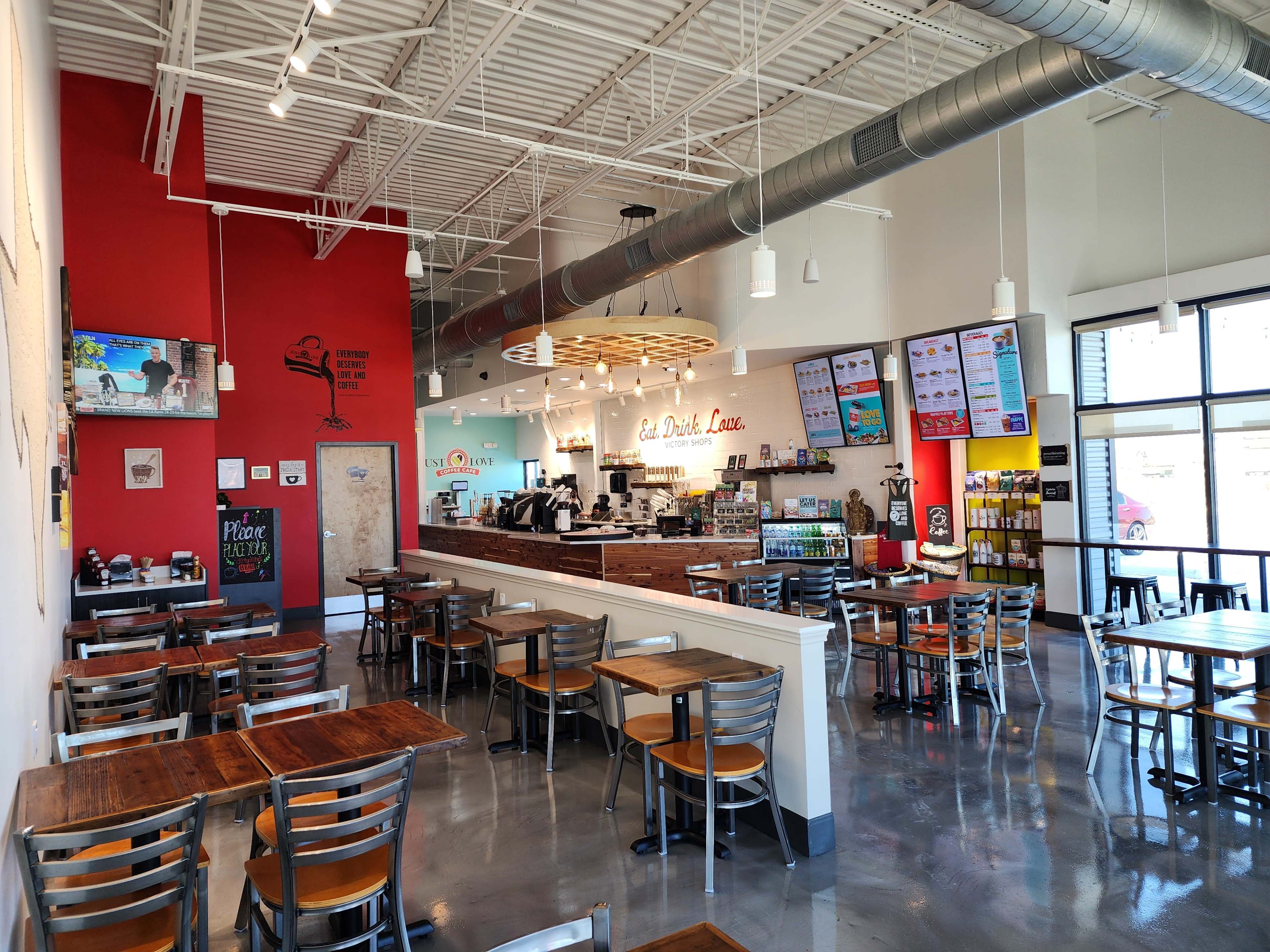 A modern café interior with wooden tables, metal chairs, a counter with a menu board, and colorful wall decorations.
